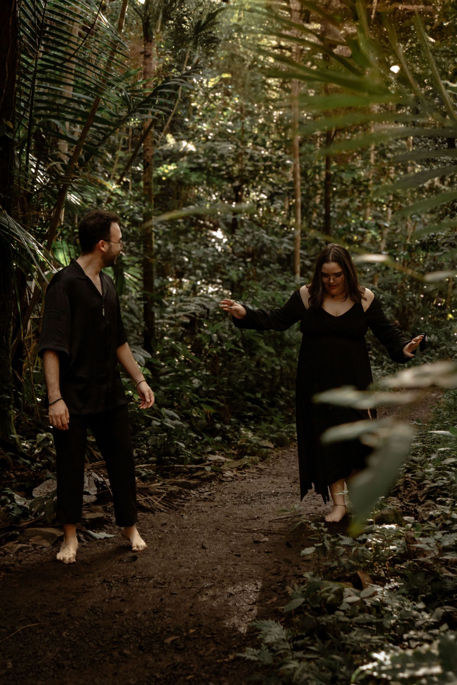 A couple walks through a lush forest path during a romantic photoshoot.