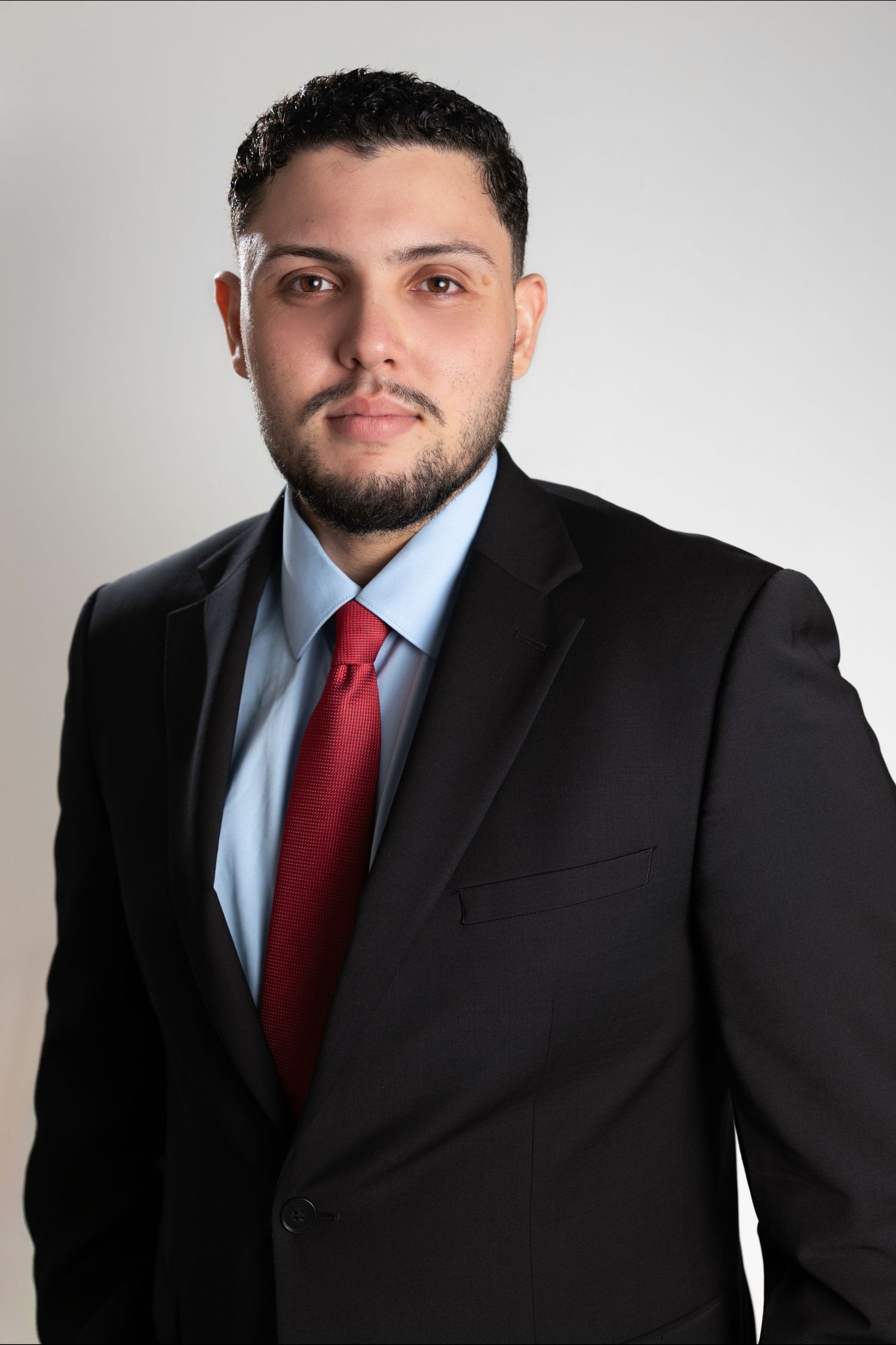 Professional headshots of person in black suit and red tie against white background.