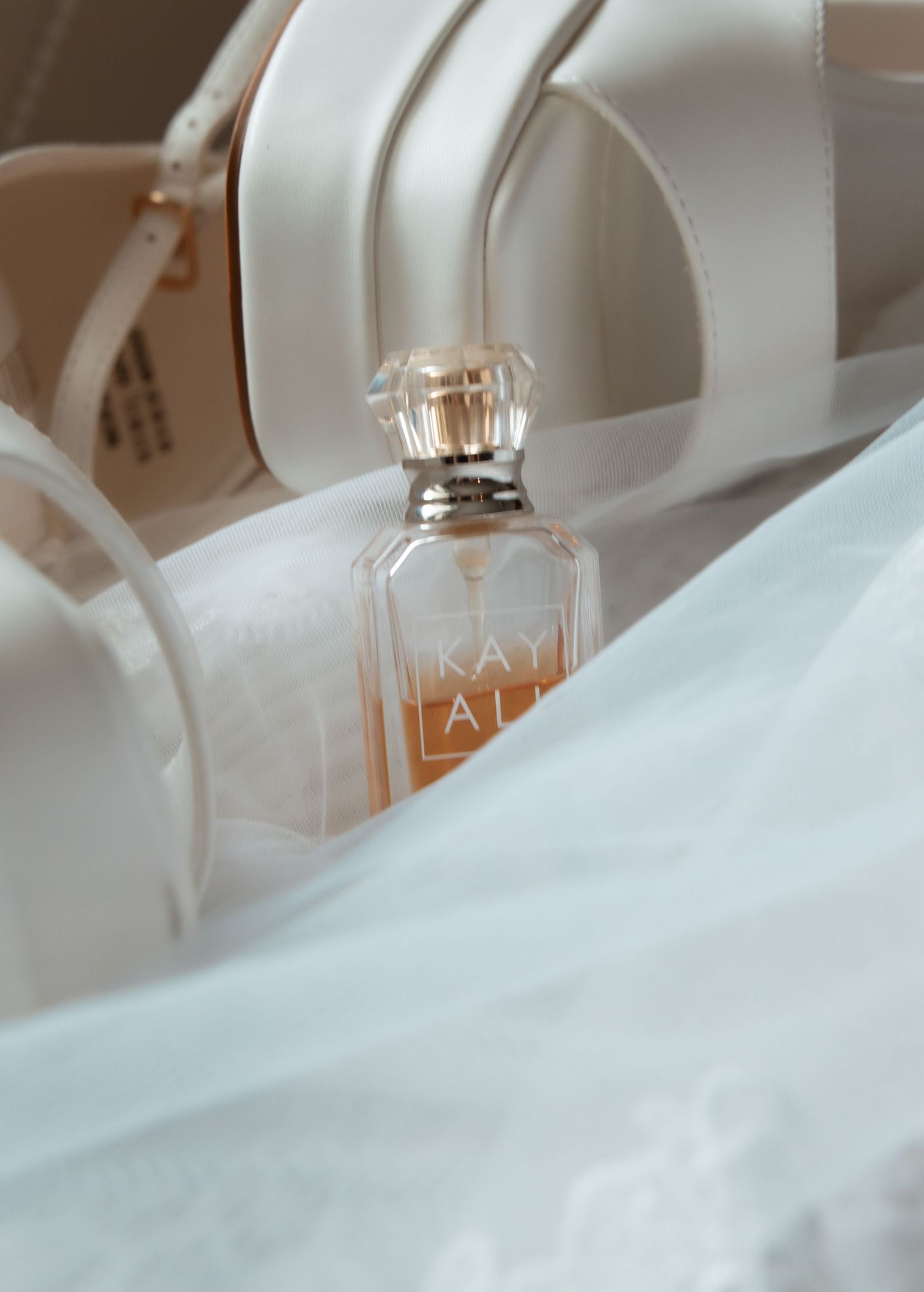 A soft and dreamy closeup of a perfume bottle with 'LA' text visible through ethereal white fabric.