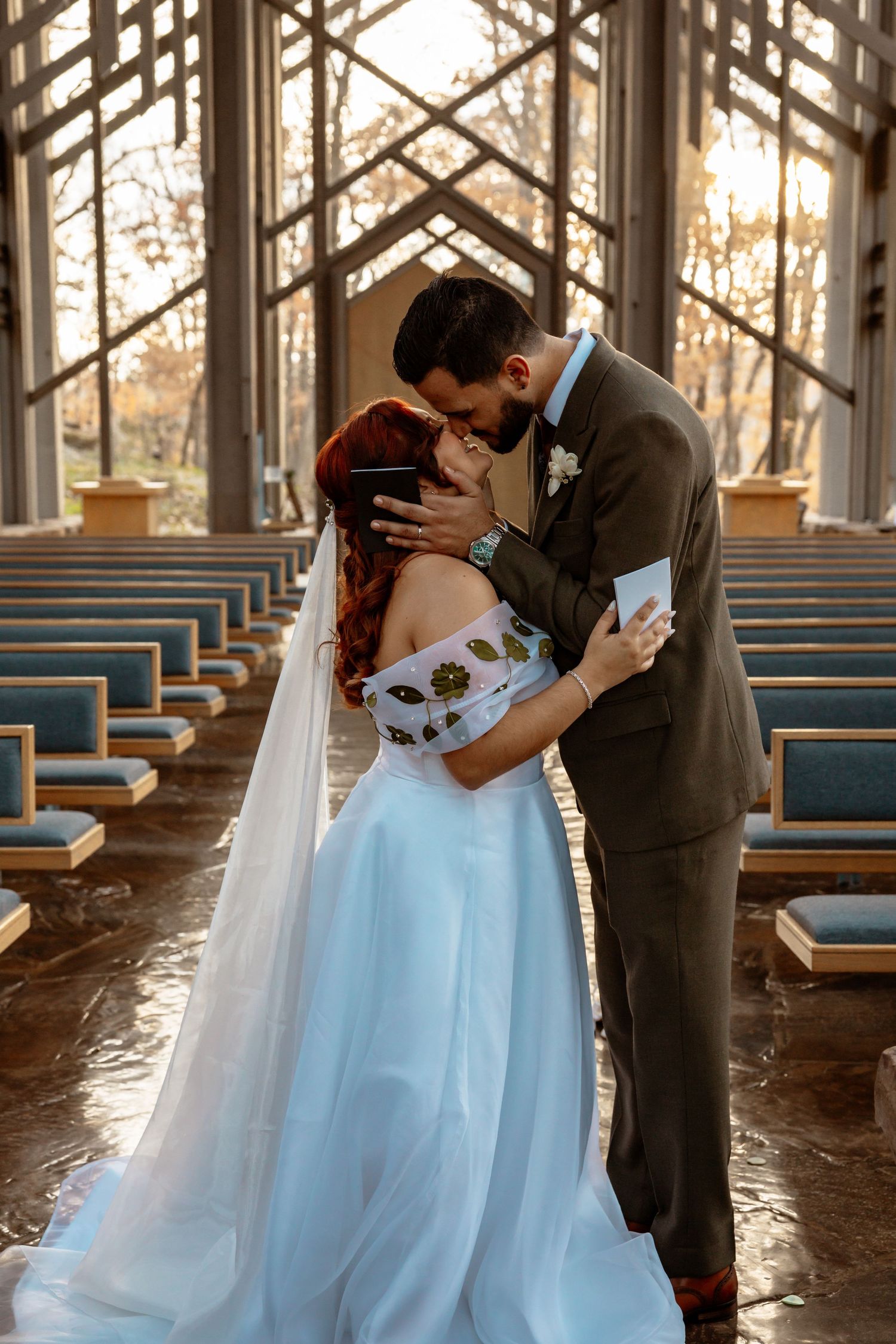 Romantic wedding moment in a sunlit chapel with wooden beams and blue pews.