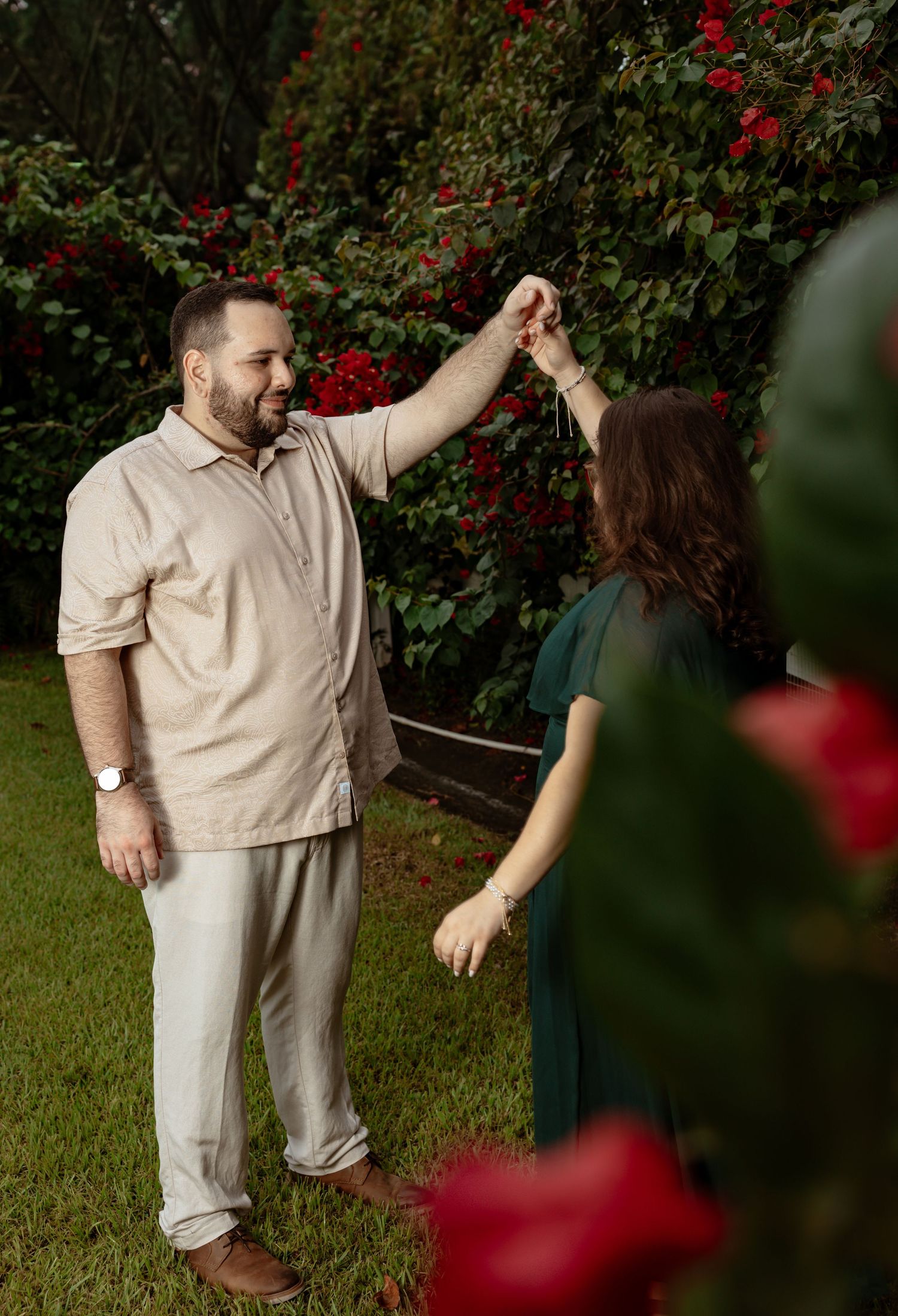 A couple dances among red flowers in a garden setting.