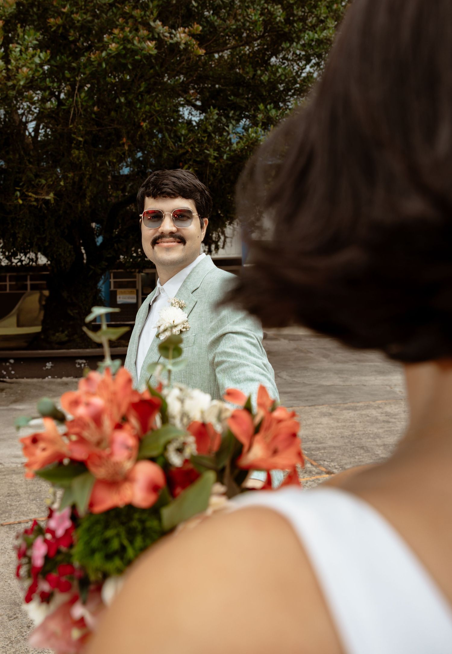 A wedding bouquet of coral and white flowers is held against a white suit jacket.