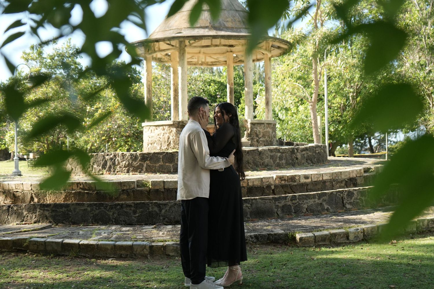Couple sharing a moment under leafy green trees in a garden setting.