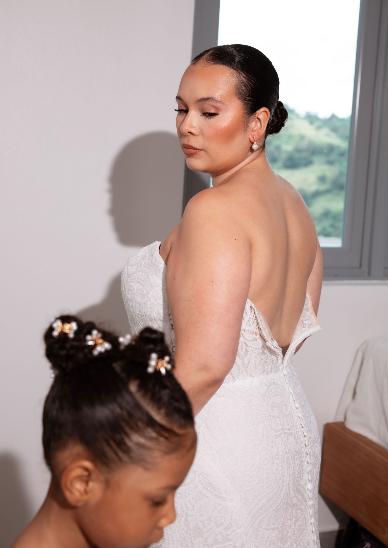 A bride in a white lace wedding dress gets ready on her special day with elegant hair styling and makeup.