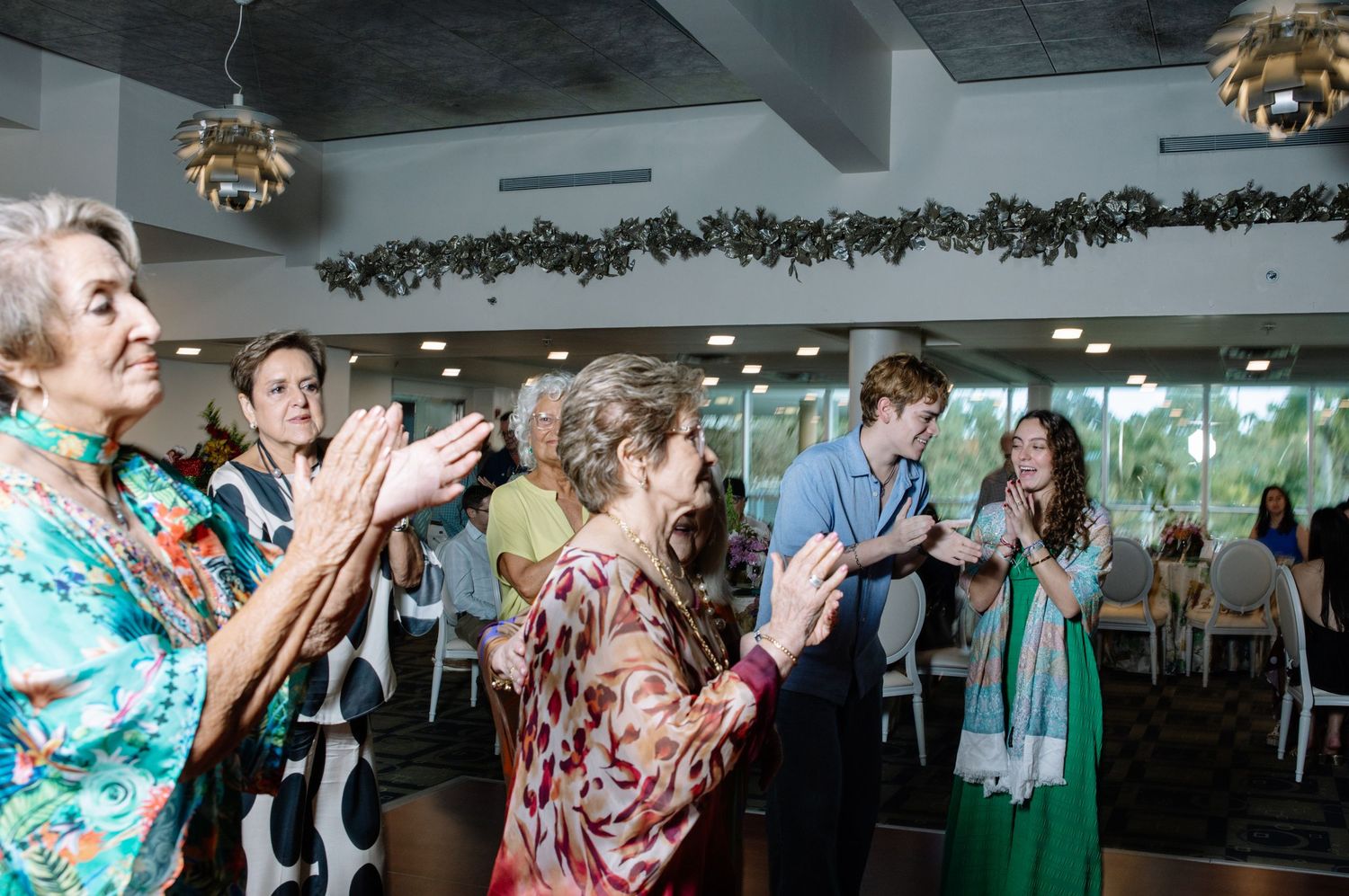 People dancing and celebrating in a large event space with decorative lighting.