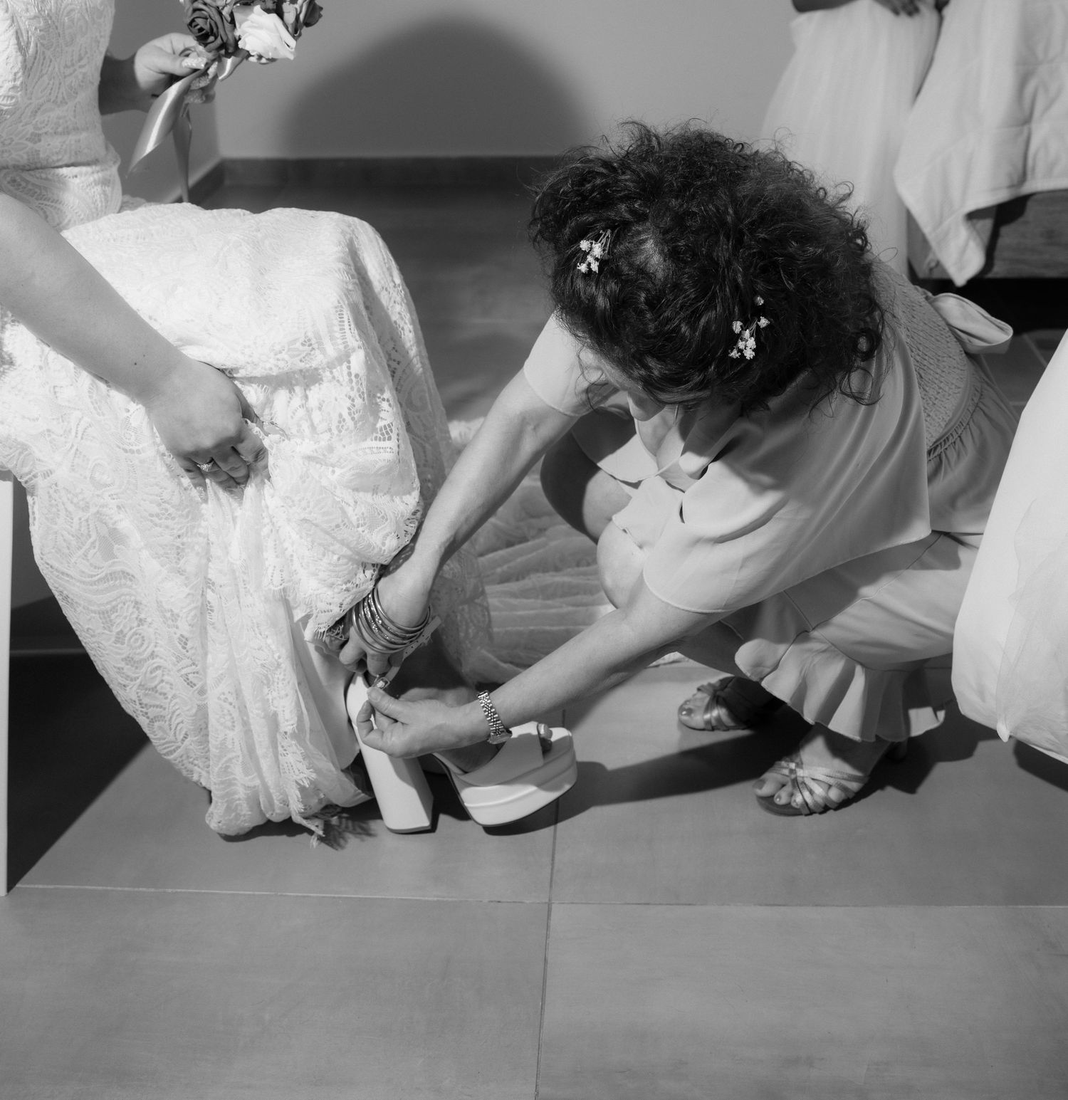 Black and white photo series showing someone putting on elegant white bridal shoes and adjusting dress details.