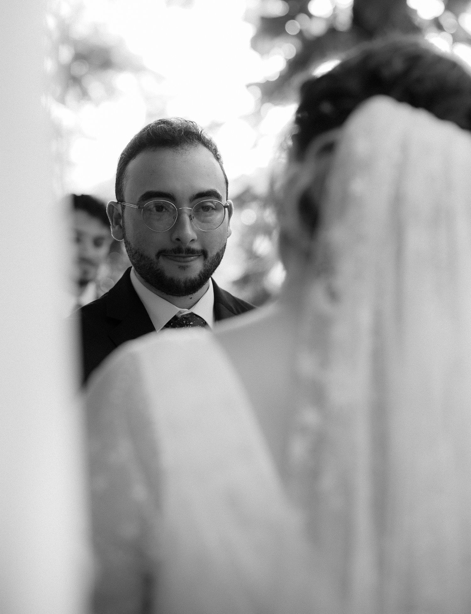 Groom in glasses smiling at bride during outdoor wedding ceremony in black and white photo.