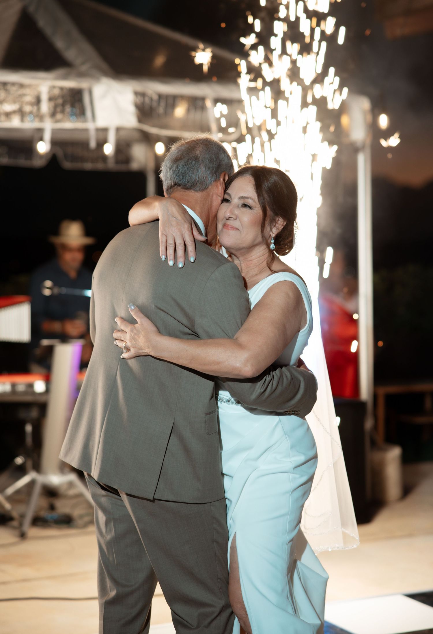 A couple shares an intimate dance moment under sparkling chandeliers at an evening reception.