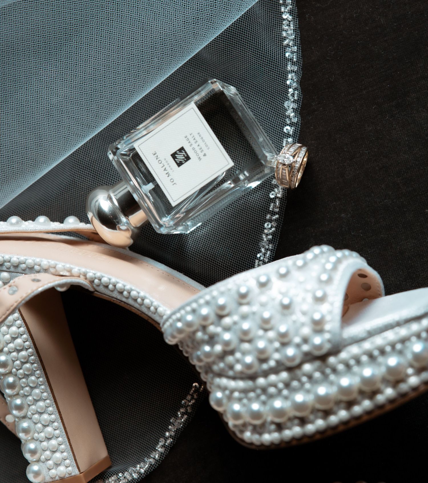 Close-up view of a decorative high heel shoe adorned with delicate pearls and crystals against a dark background.