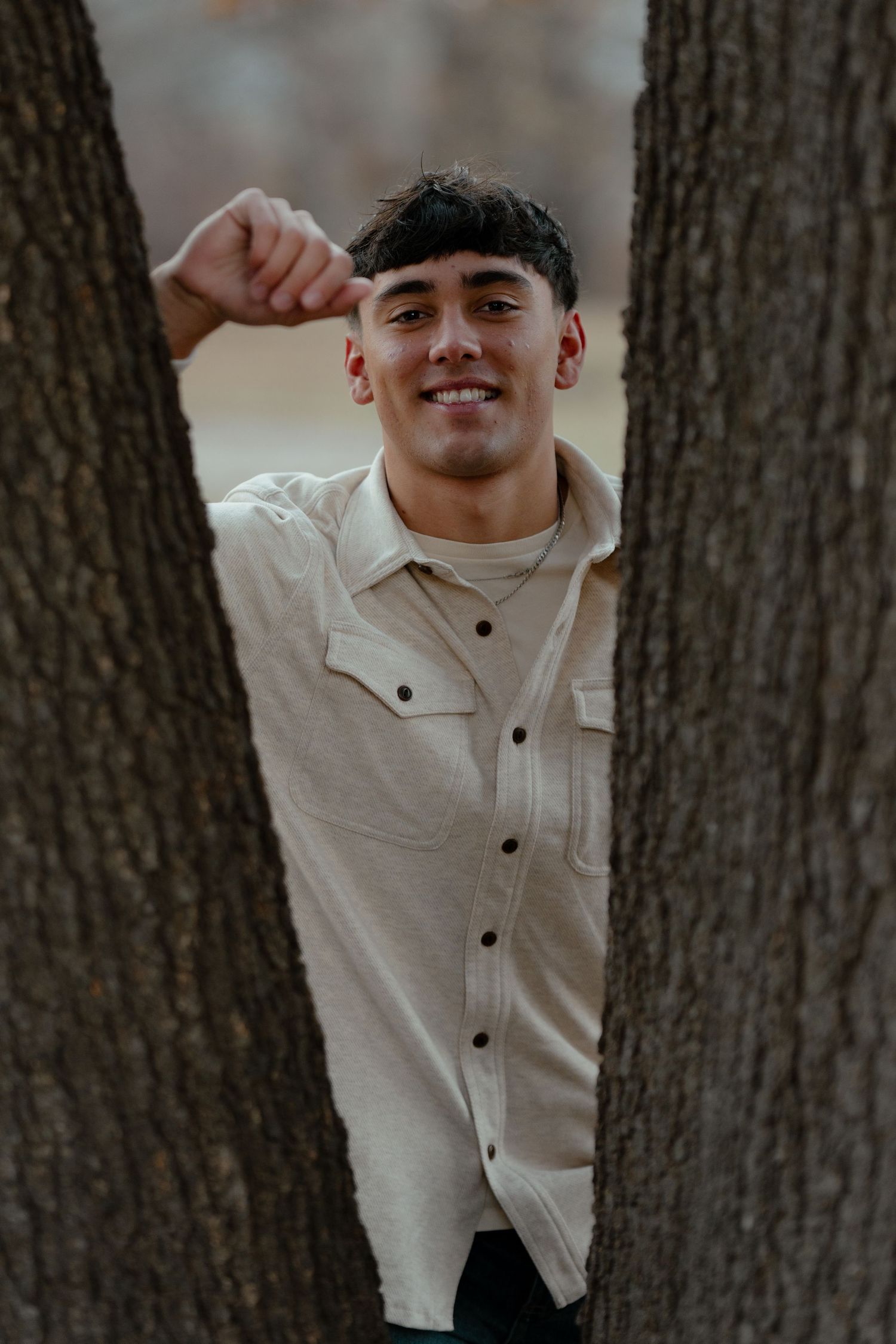 Playful outdoor portrait between tree trunks wearing a cream button-up jacket.