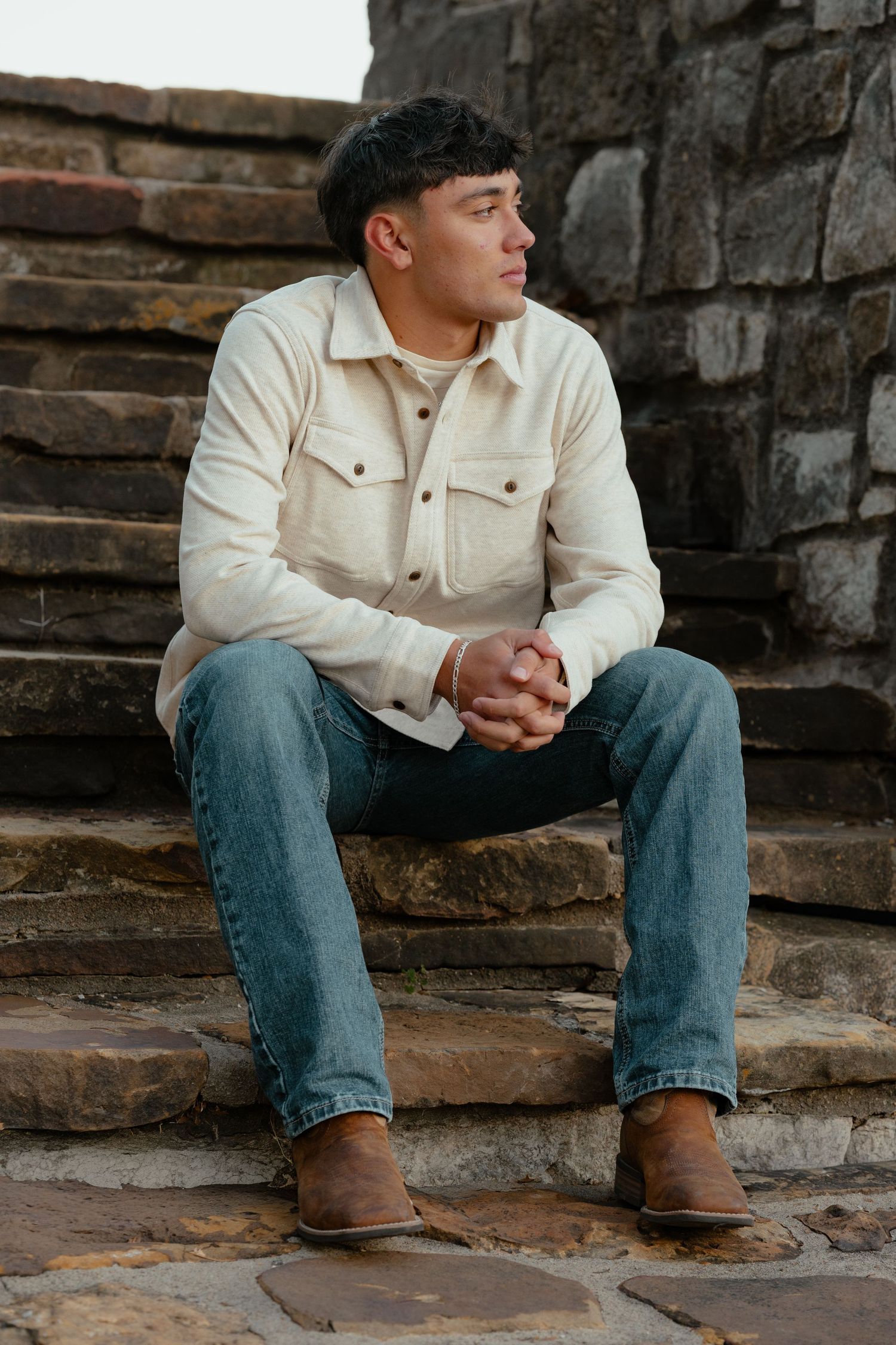 Person in white jacket and jeans sitting on stone steps.