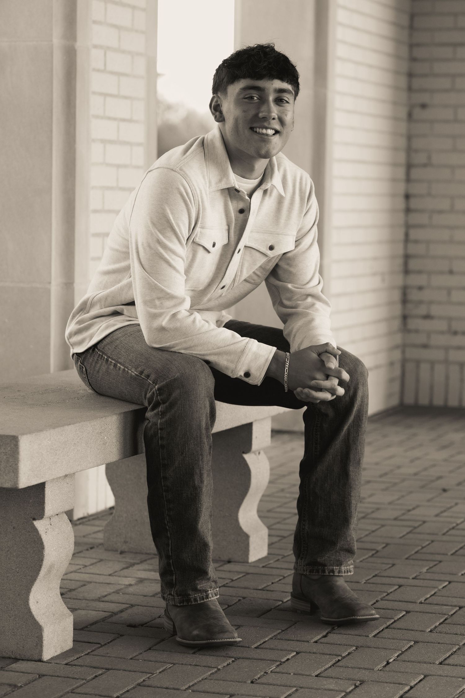 A monochrome photo of someone seated on brick steps wearing jeans and a white shirt.