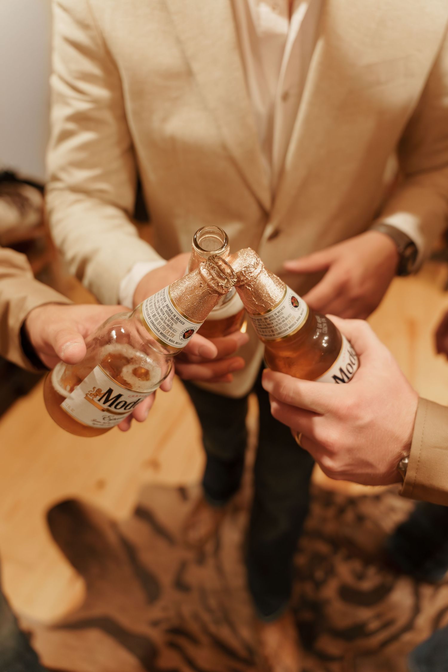 People clinking Modelo beer bottles together in a celebratory toast at a formal event.