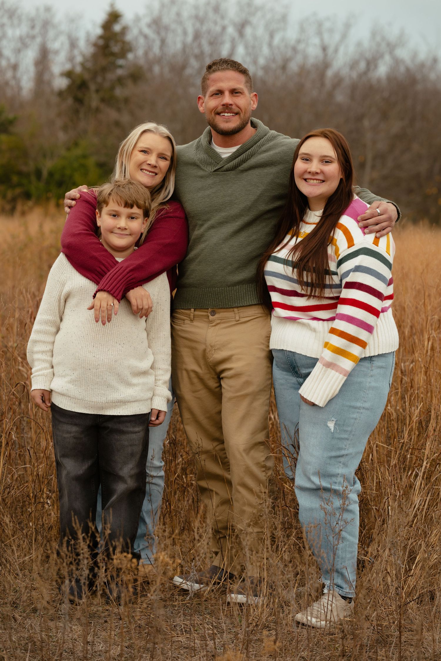 A family stands together in a field of tall brown grass during a casual outdoor photo session.