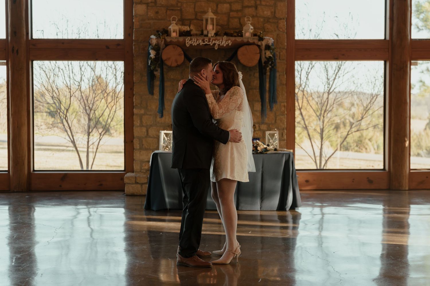 A couple dances together in an elegant ballroom with wooden floors and large windows overlooking a scenic landscape.