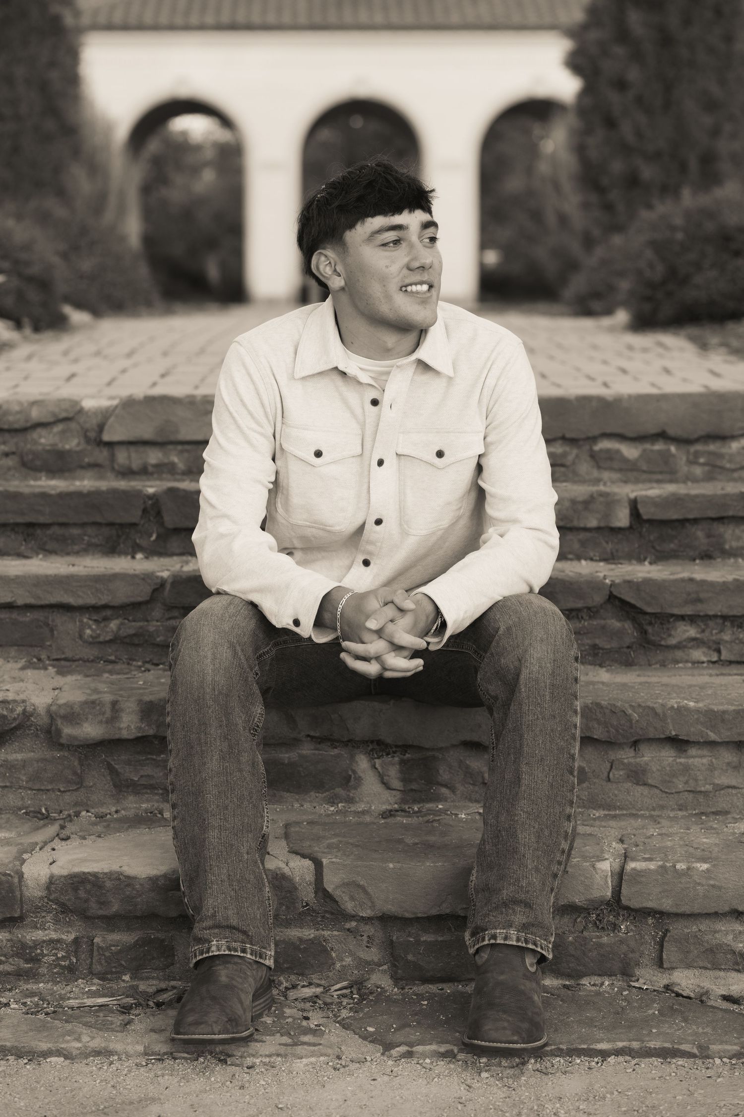 A black and white photo of someone seated on stone steps with arched architecture visible behind.