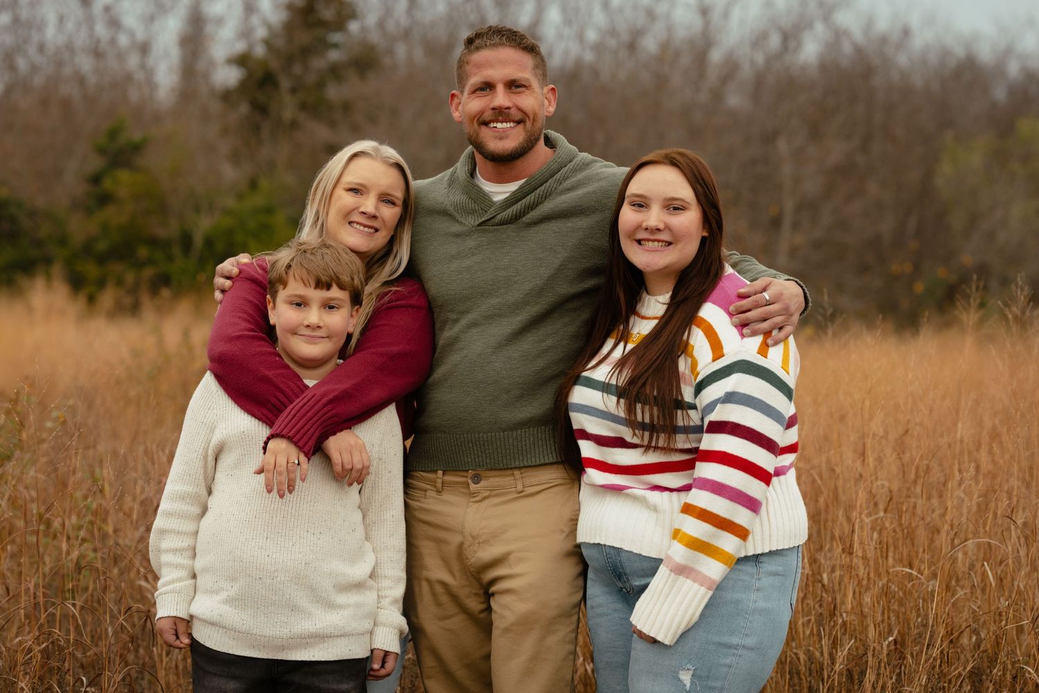 Family members embrace while standing in a golden field during sunset.