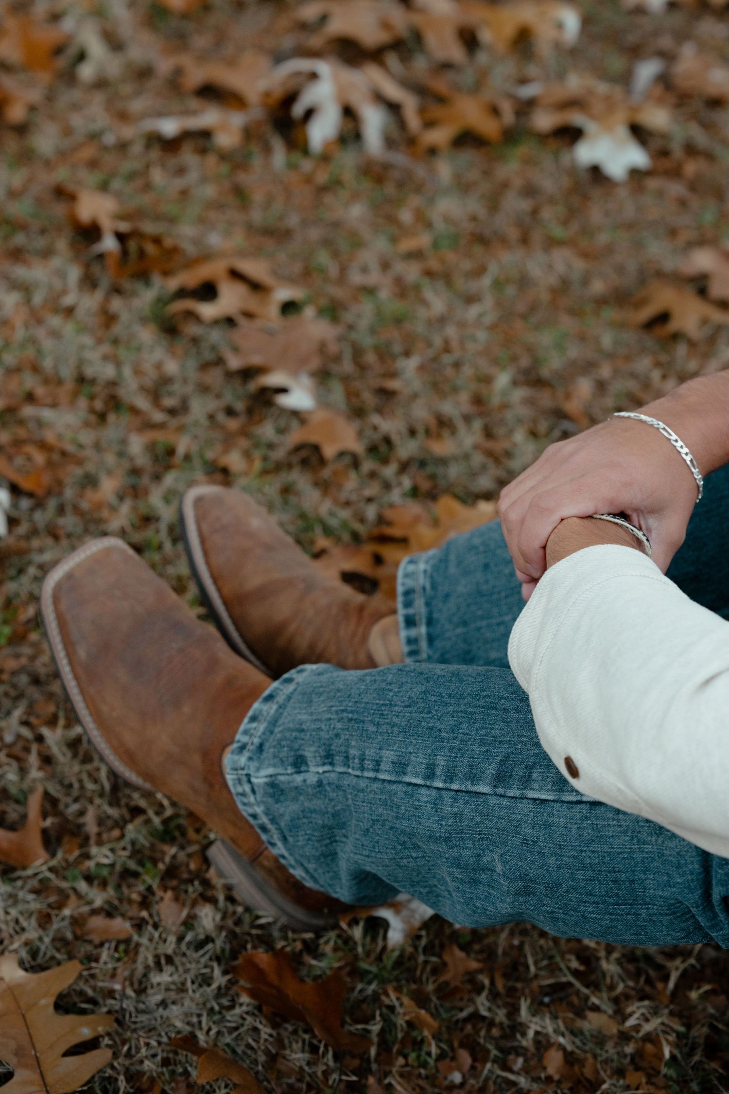 Close-up of brown boots and blue jeans with fall leaves scattered on the ground.