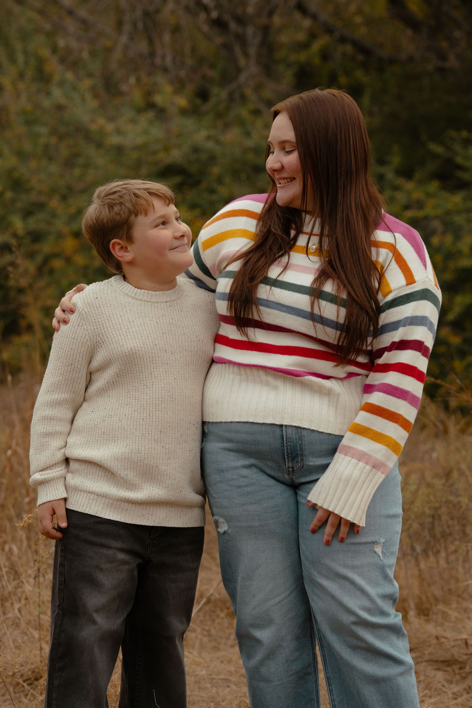 A family poses playfully in a field during an autumn photoshoot wearing coordinated casual outfits.
