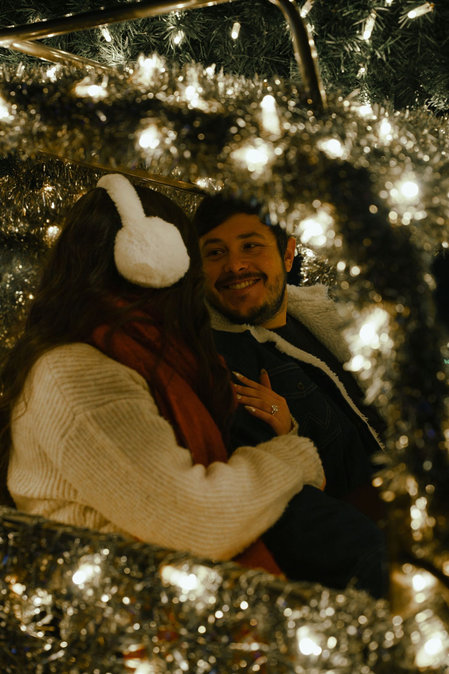 A couple shares a tender moment under twinkling Christmas tree lights creating a warm and intimate holiday atmosphere.