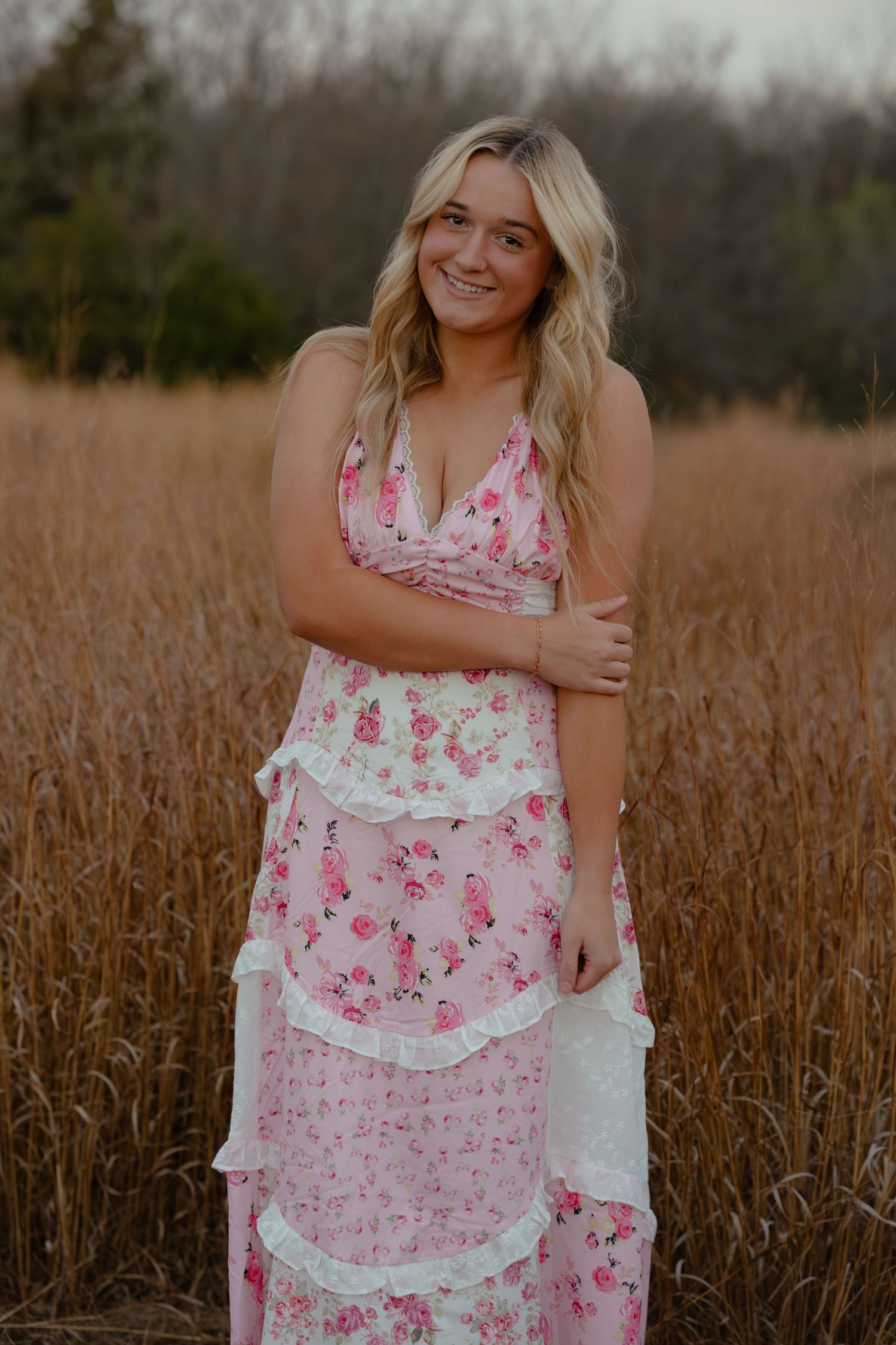 Young blonde woman in pink floral tiered maxi dress smiling in a golden wheat field.