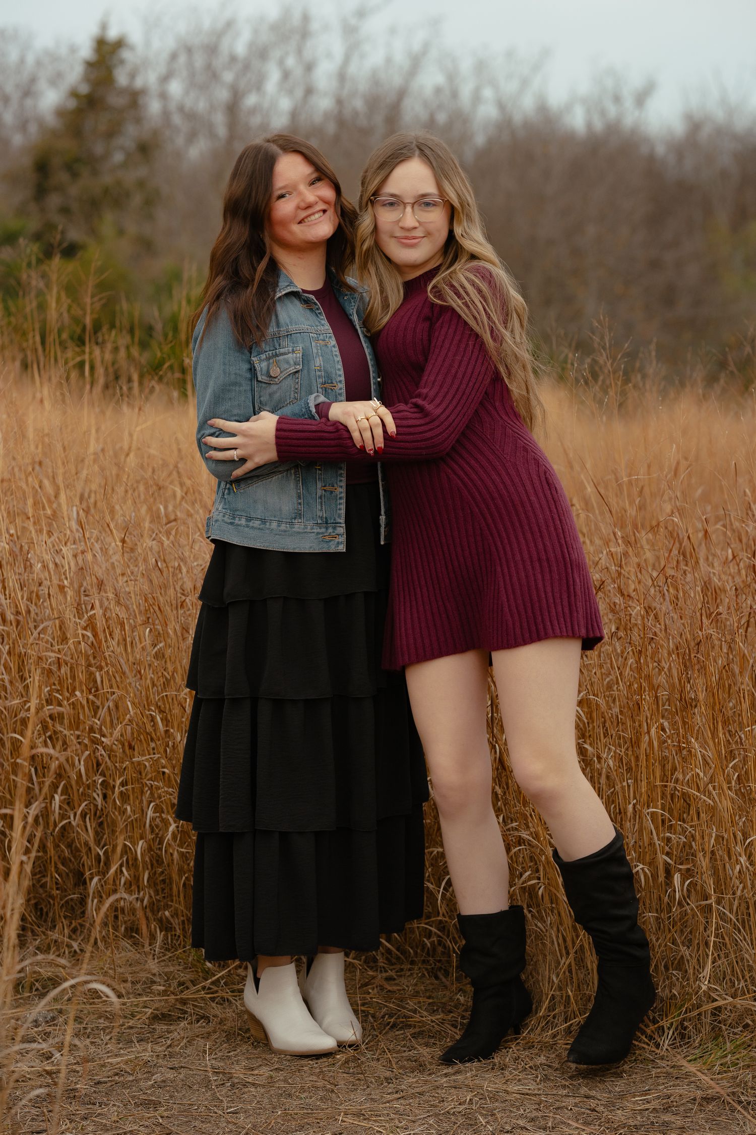 Friends in contrasting outfits embrace while standing in autumn field.