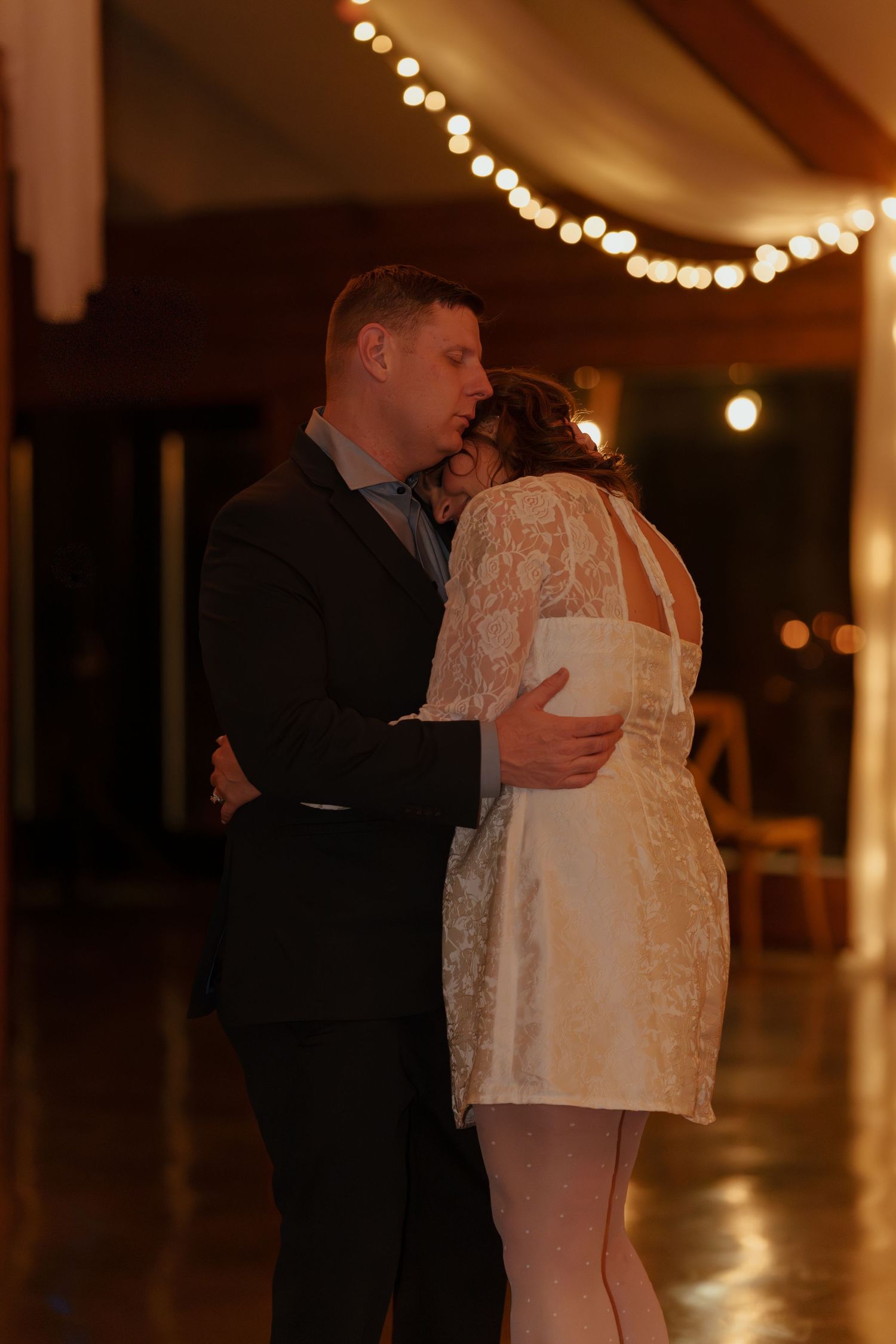 A romantic slow dance moment captured under warm string lights at a wedding reception.