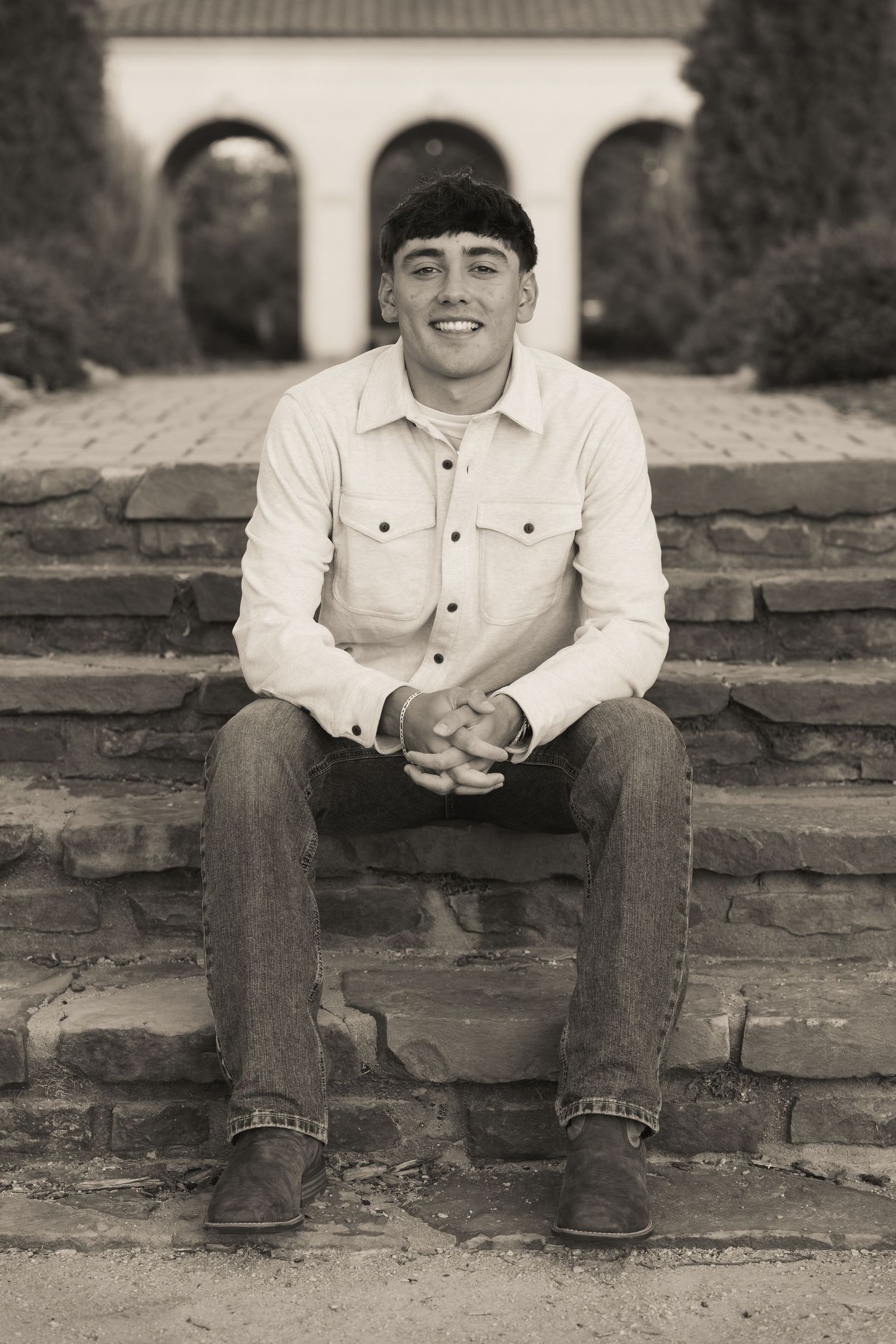 A black and white photo of someone sitting on stone steps wearing western casual attire.