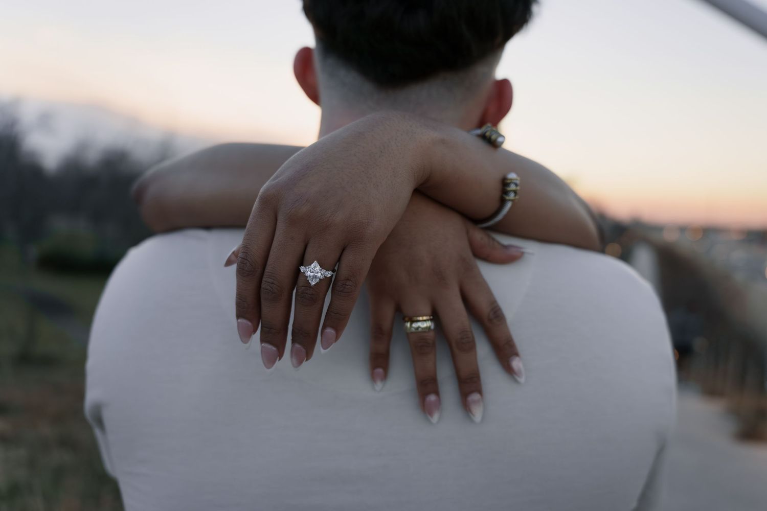 A close-up sequence of hands displaying engagement rings against a blurred outdoor background at sunset.