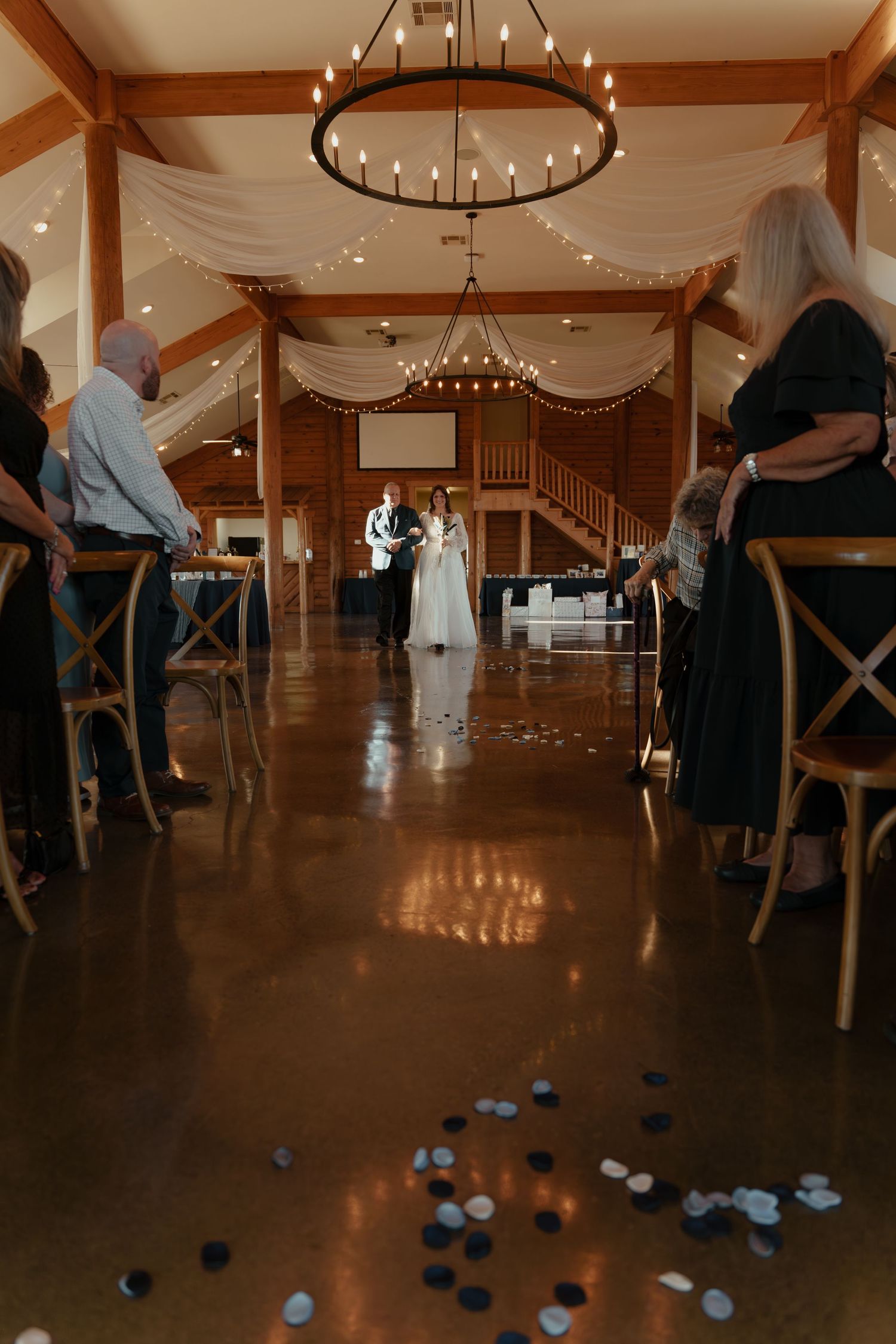 Indoor bocce ball game in progress on wooden floors of rustic event venue with circular chandeliers overhead.