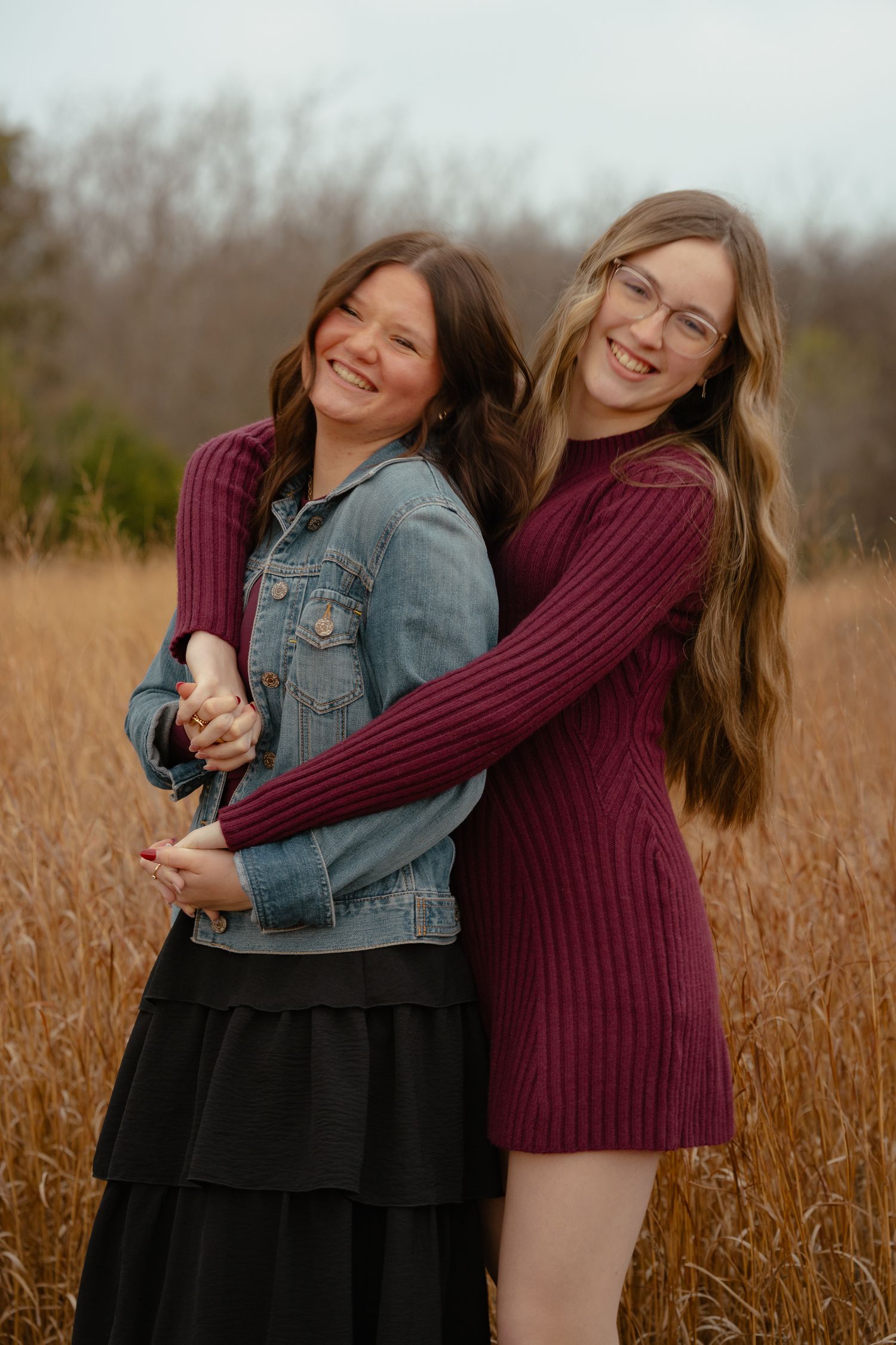 Two friends embracing and laughing together in a field of tall grass at sunset.