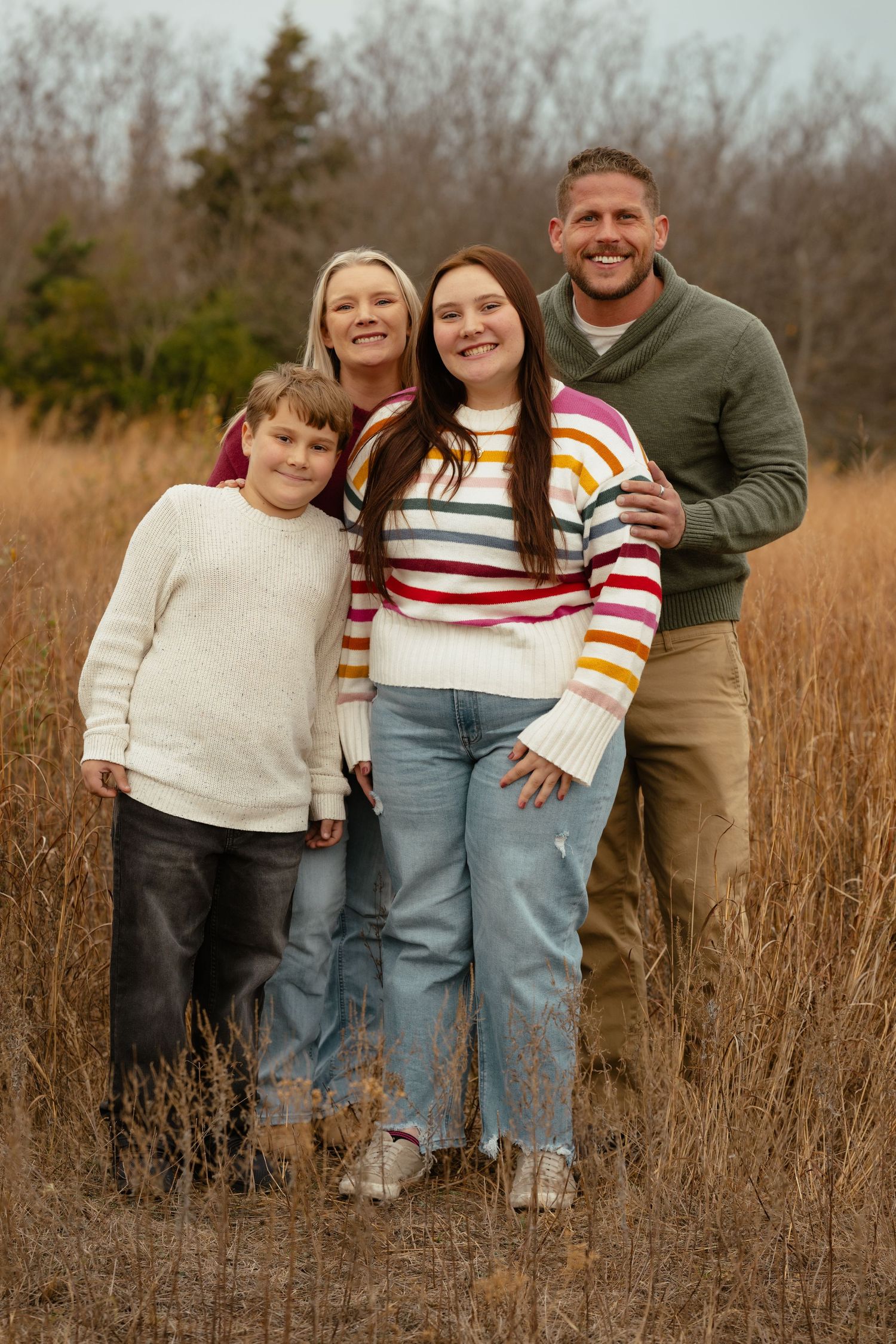 Family members pose casually together in a field with autumn foliage.