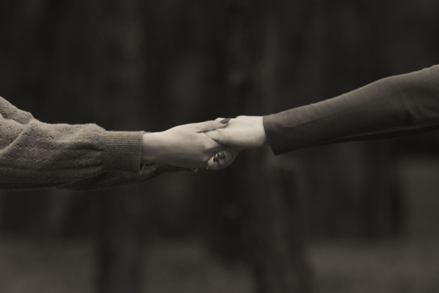 Black and white artistic photo of hands reaching towards each other.