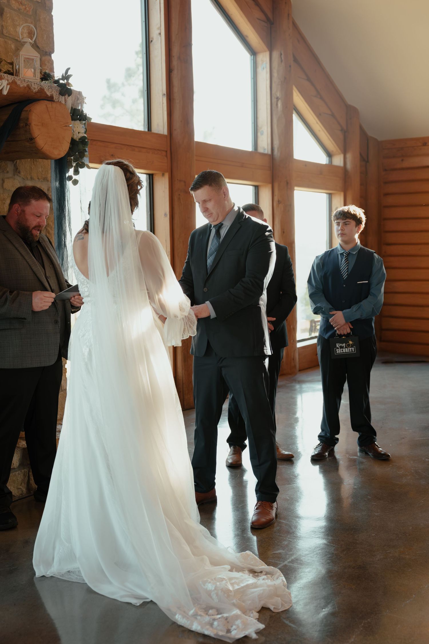 Bride and groom exchange vows at indoor rustic wedding ceremony in wood-paneled venue with large windows.