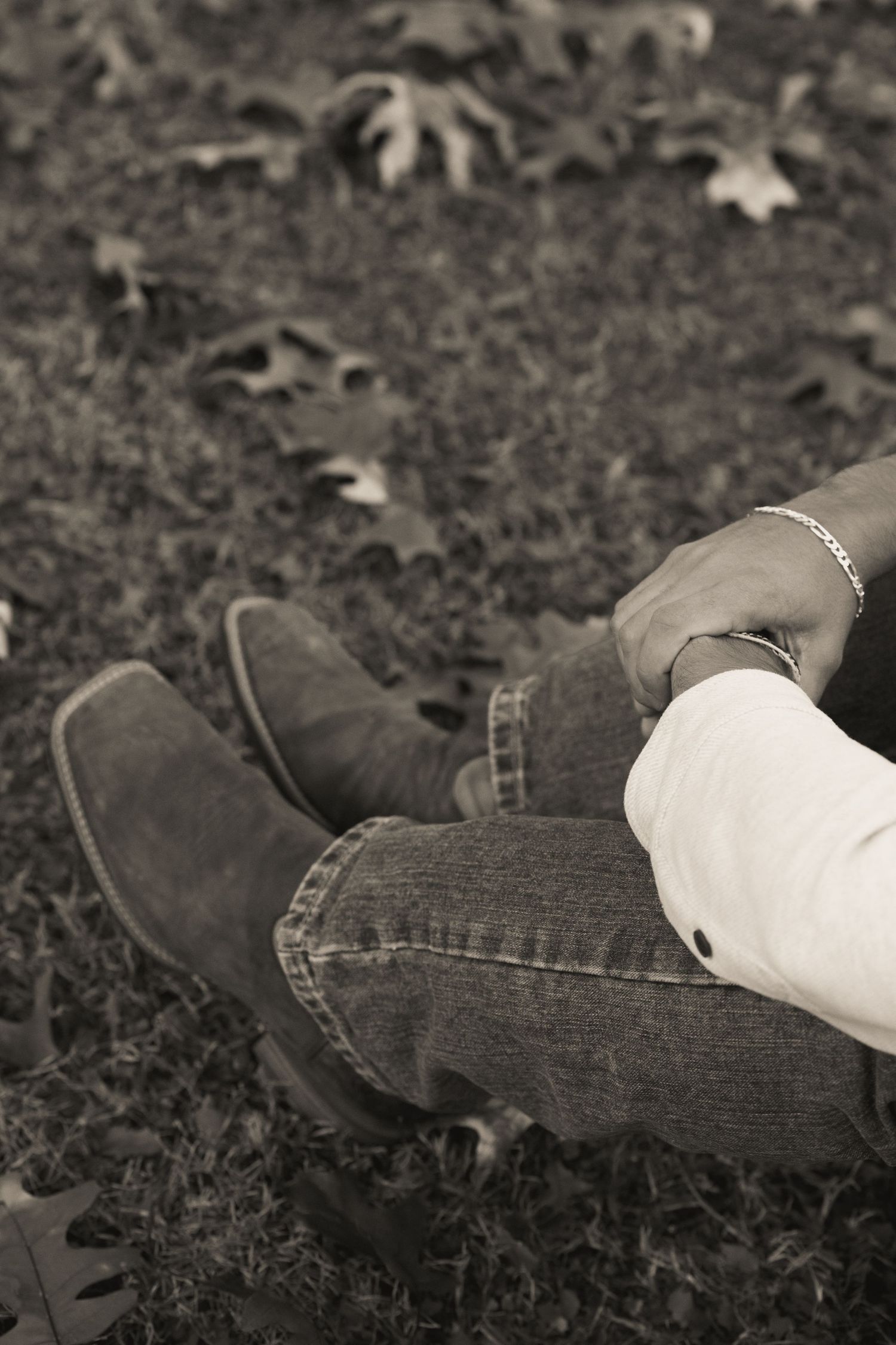 Black and white detail shot of boots and jeans with scattered autumn leaves on ground.
