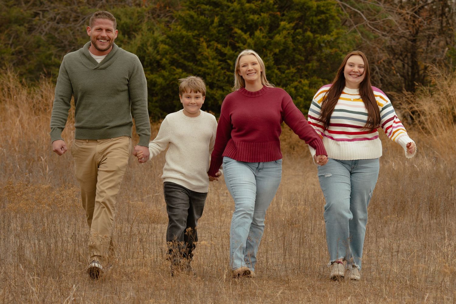 Family members walk hand in hand through tall grass during an outdoor photo session.