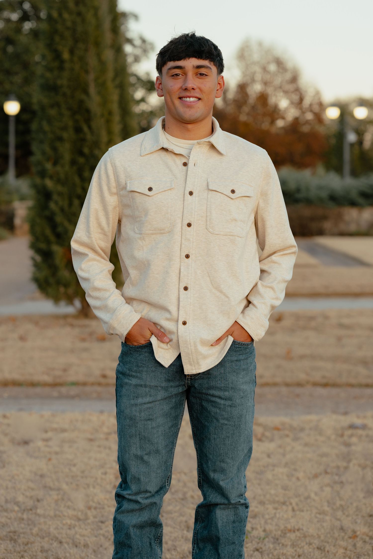 A casual outdoor portrait featuring a cream jacket and blue jeans against a natural background.