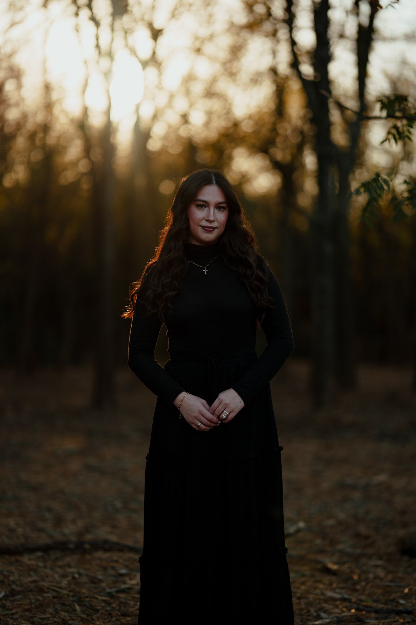 Moody sunset portrait of person in black dress walking through autumn woods.
