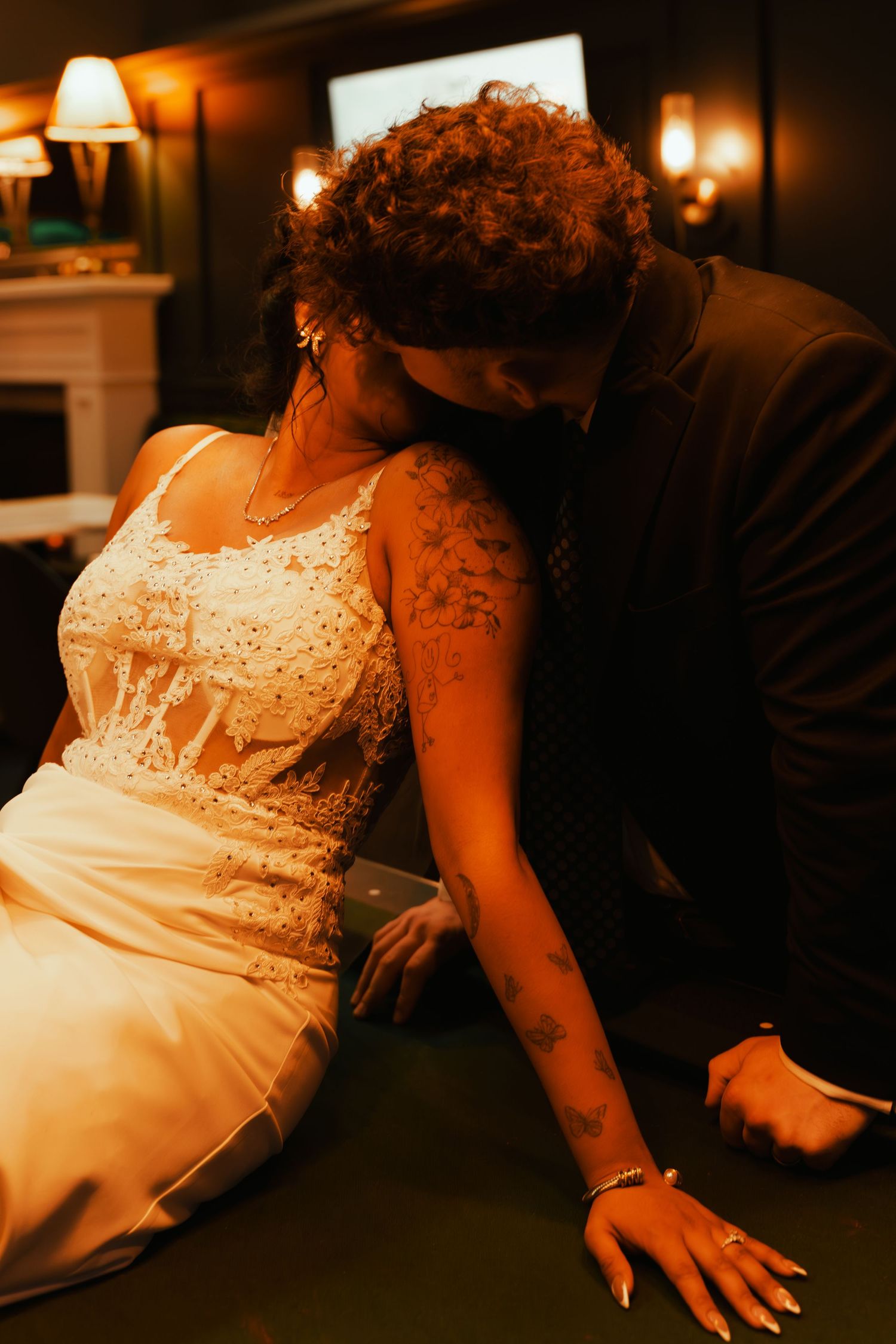 A romantic evening scene showing someone in a white lace dress sitting on a dark couch in warm lighting.