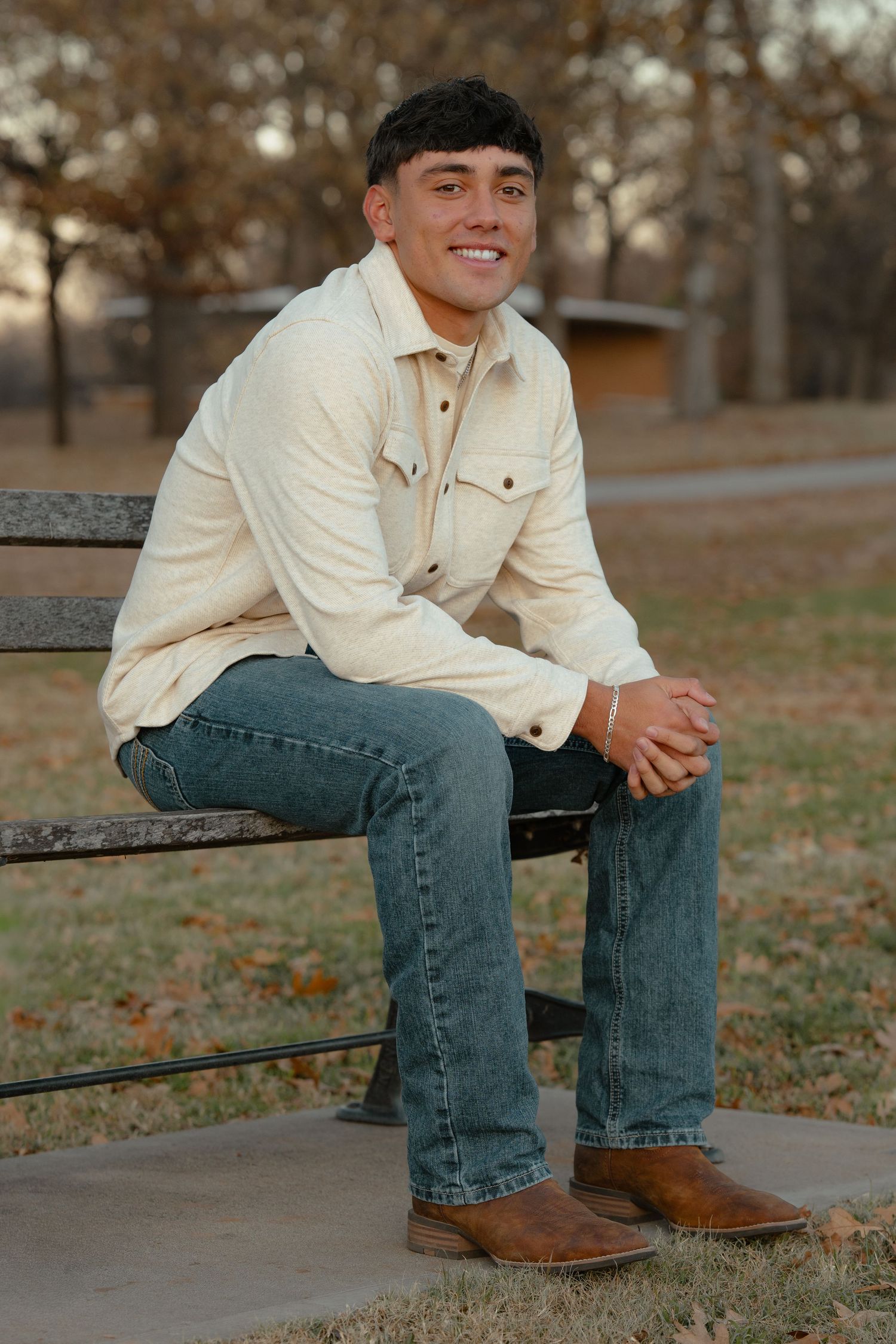 Outdoor autumn portrait of someone sitting on a bench wearing a cream jacket and jeans.
