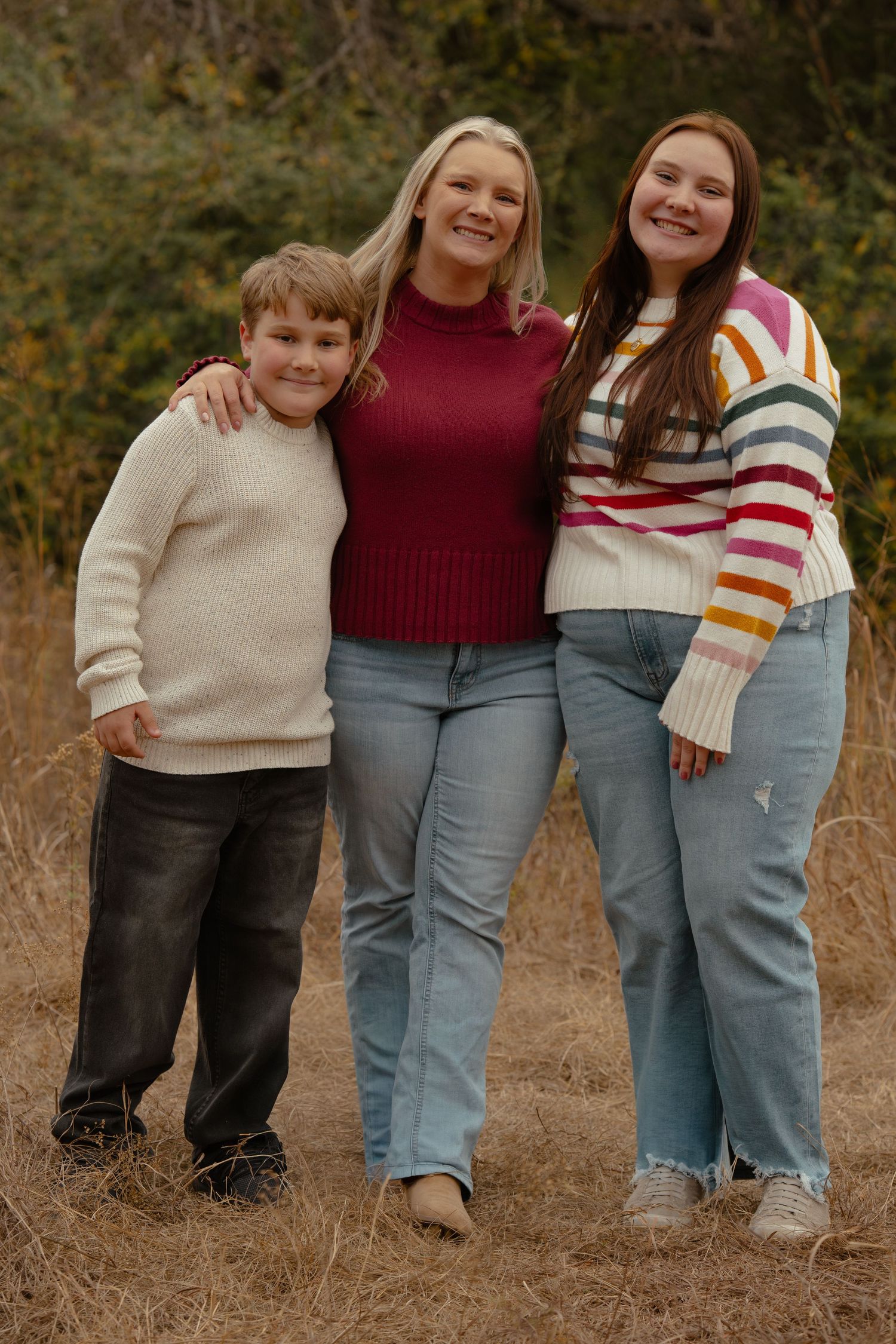 Family group posing together in coordinated casual outfits against fall foliage.