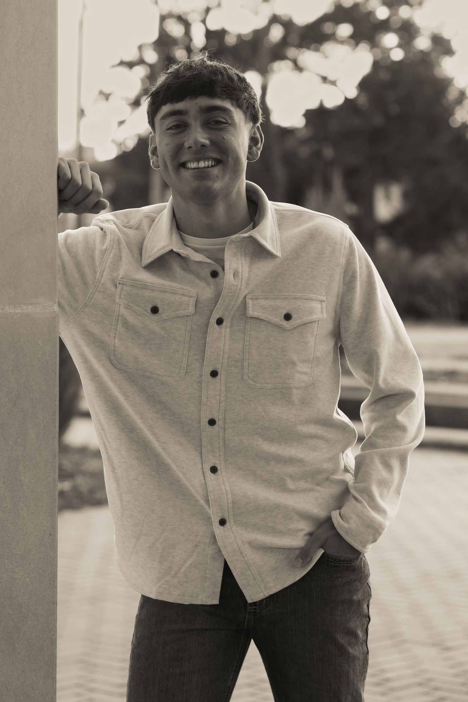 A black and white portrait of someone wearing a light-colored button-up shirt against an outdoor background.