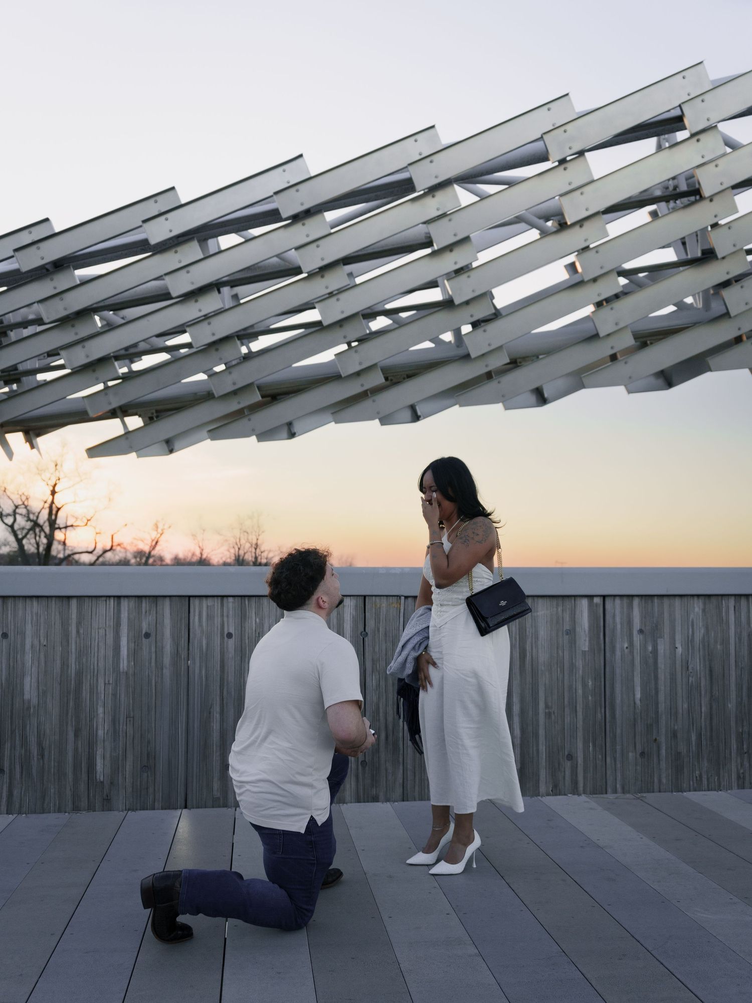 Two people relax on wooden benches at sunset beneath angular metal beams creating geometric shadows.