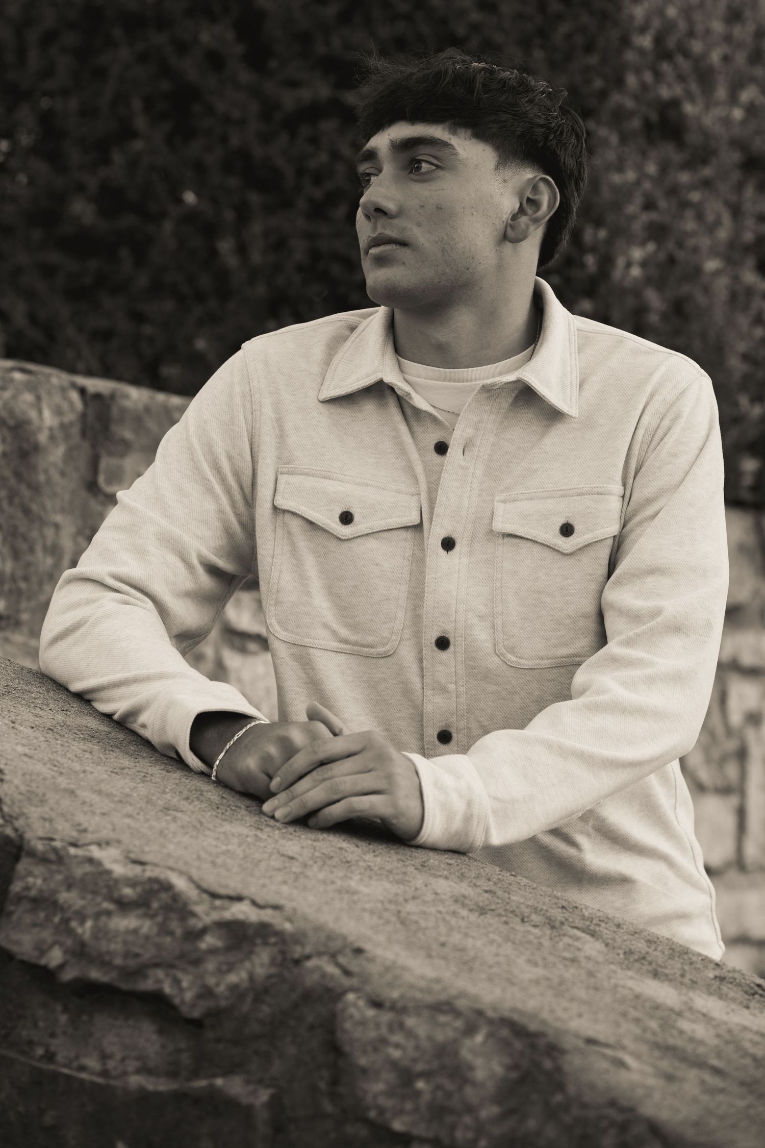 Black and white portrait of someone resting against a stone surface wearing a light jacket.