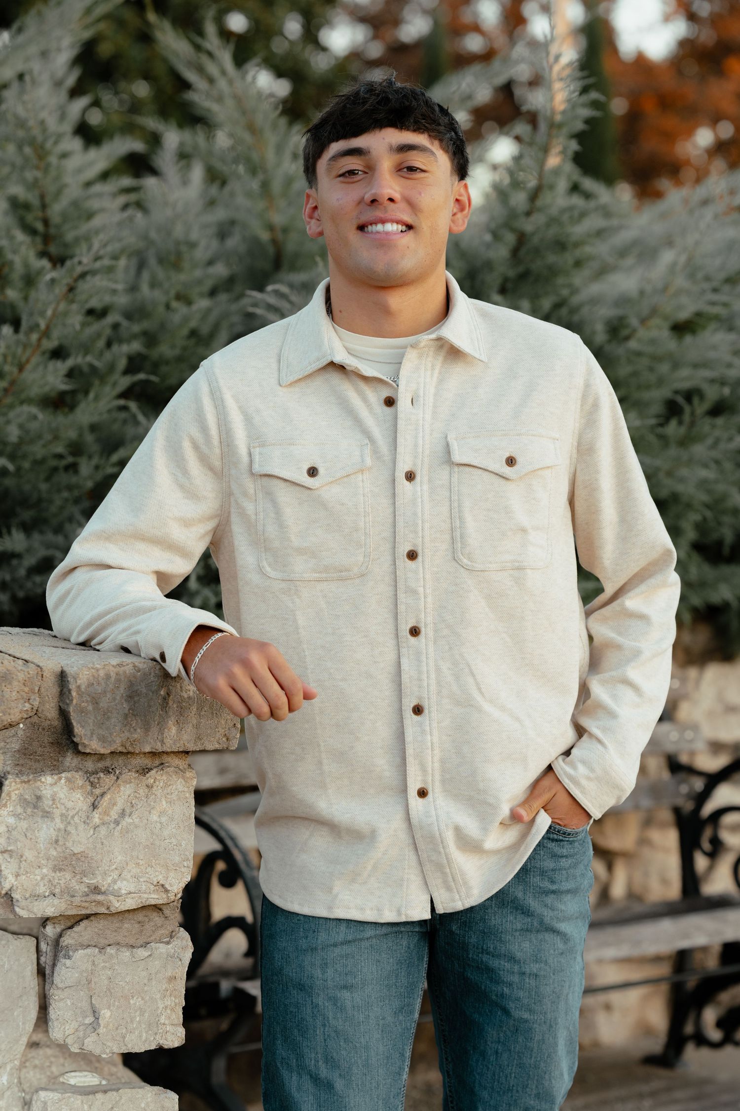 A casual outdoor portrait with someone wearing a cream jacket while standing next to a stone wall.