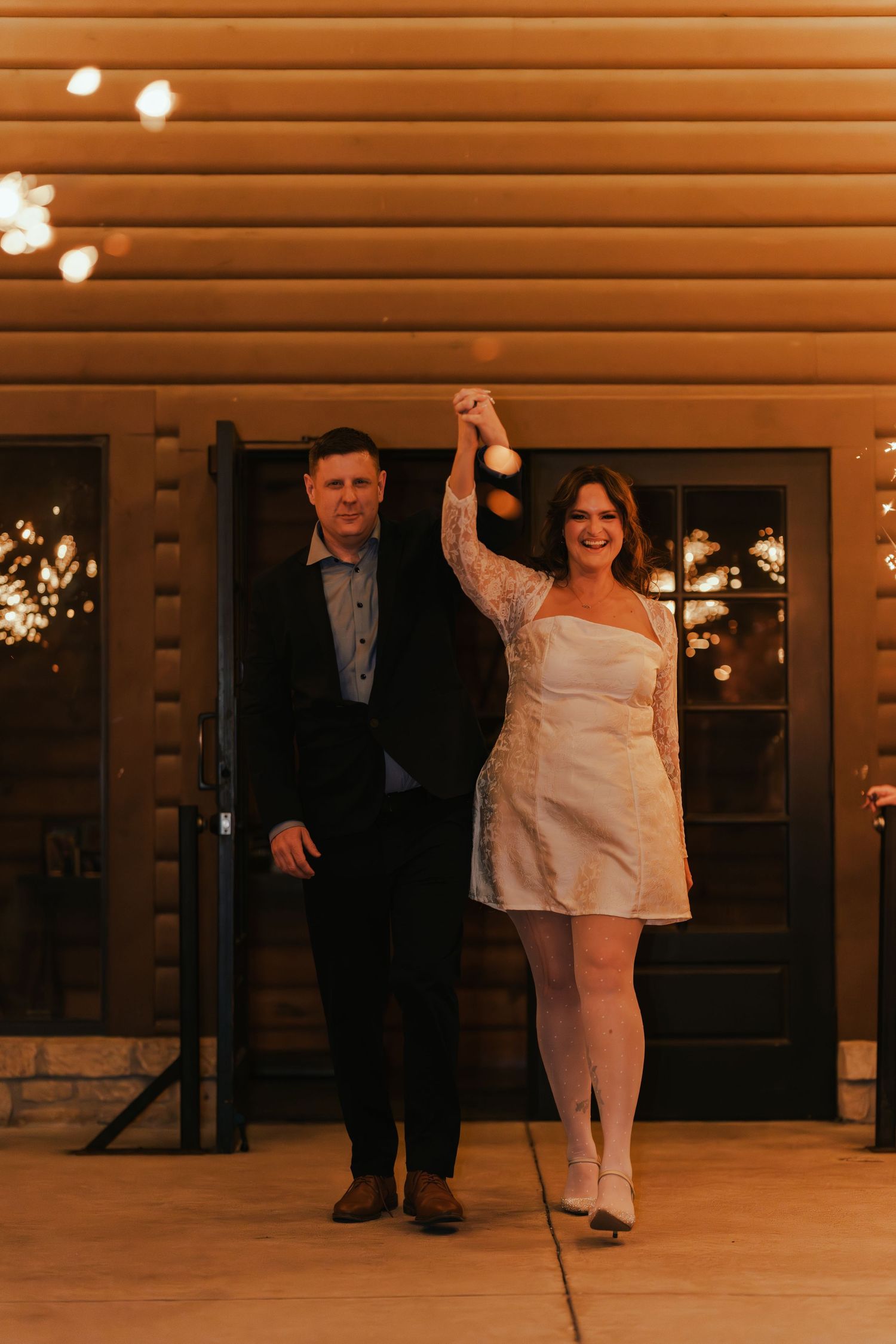 Wedding couple dances in a rustic venue with wood paneled walls and string lights.