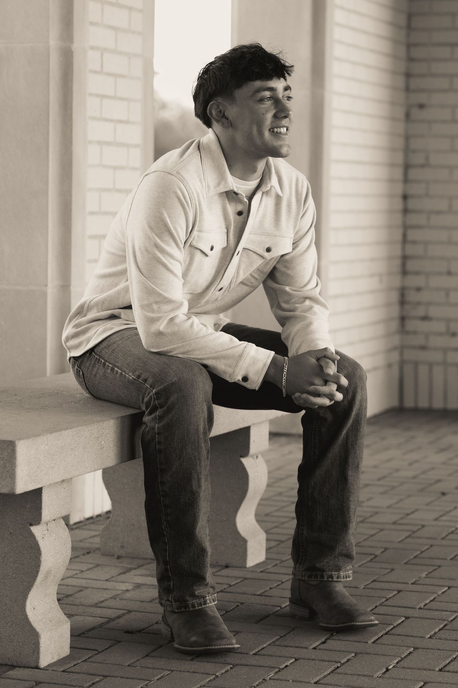 A black and white portrait of someone seated on outdoor steps.