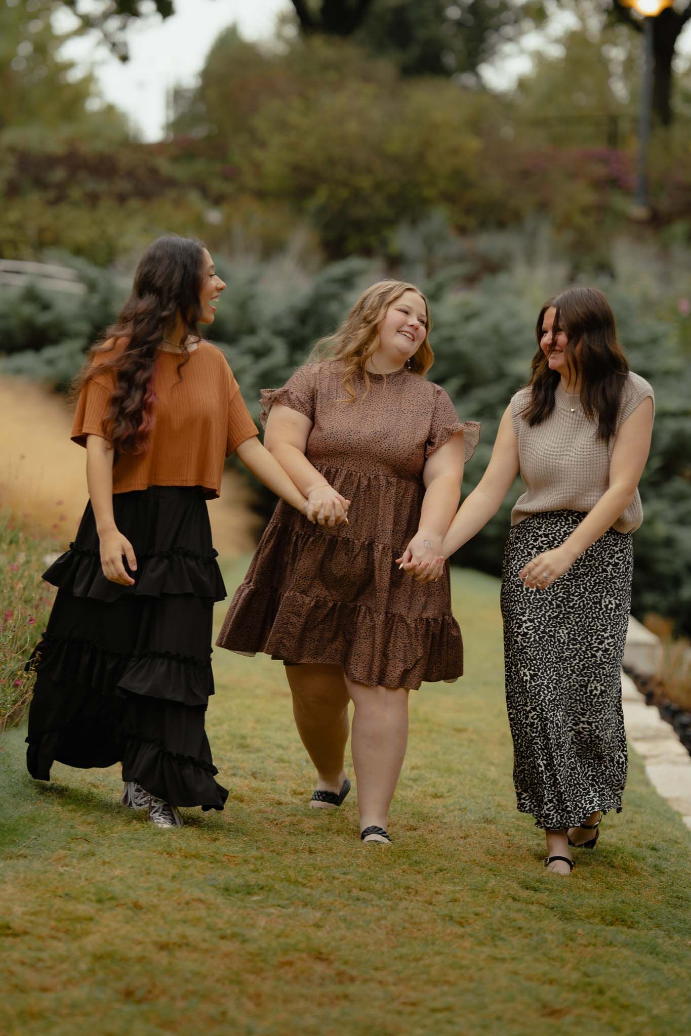 Friends holding hands and dancing together on grass during sunset.