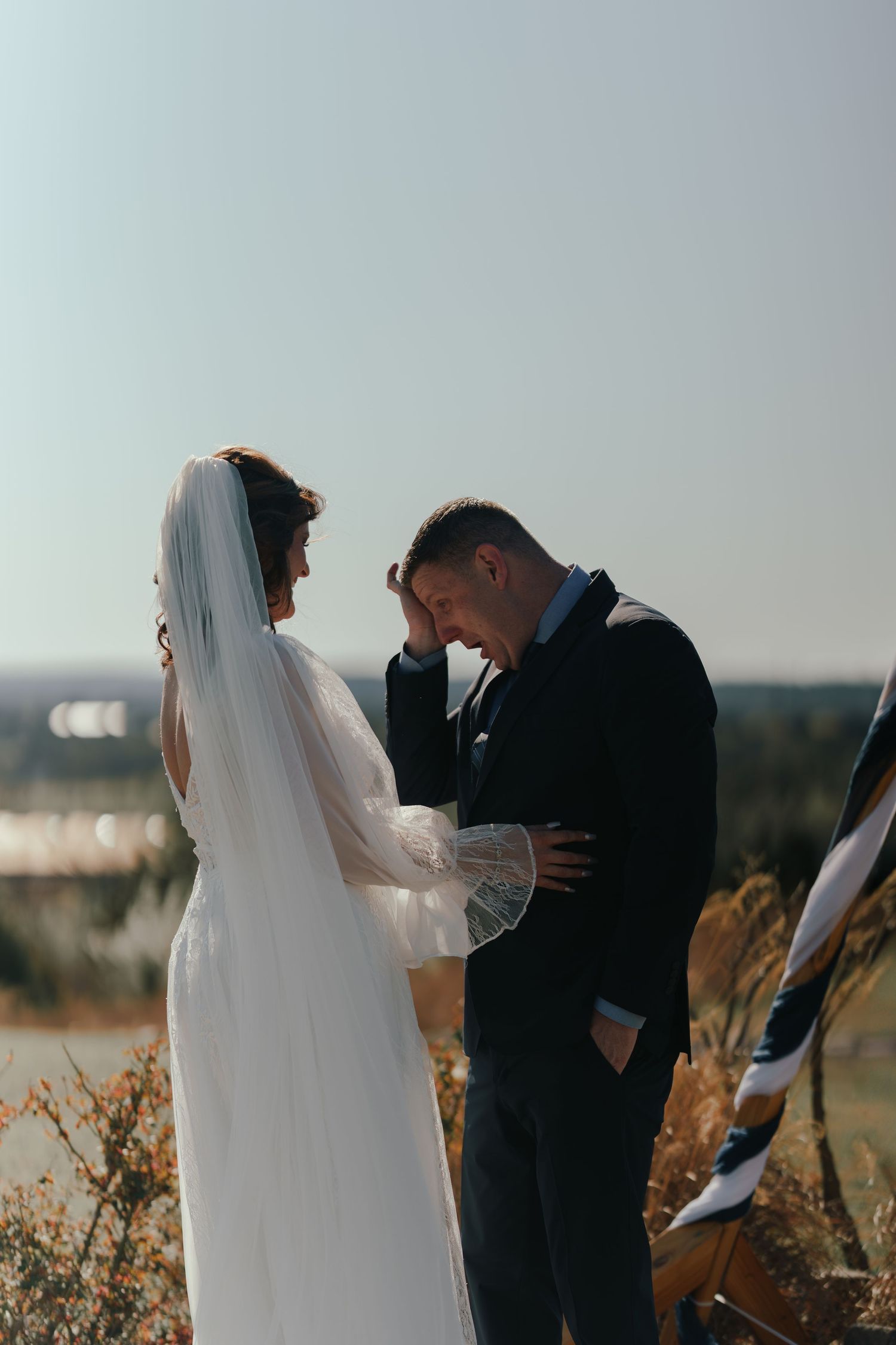 A couple in wedding attire shares an intimate moment in a golden field during their outdoor ceremony.