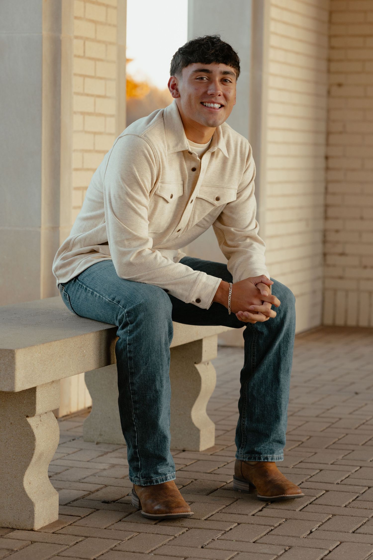 A casual portrait of someone in western attire sitting on brick steps.